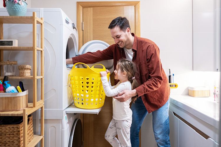 Mit energieeffizienten Geräten schonst du dein Konto Vater und Tochter holen legen Wäsche in die Waschmaschine