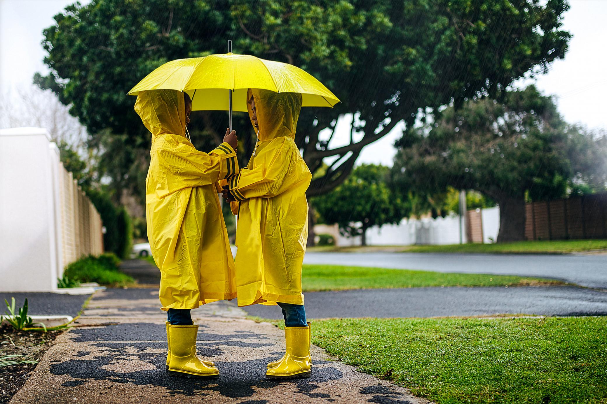 Zwei Mädchen in gelben Regenmänteln halten zusammen einen Regenschirm  