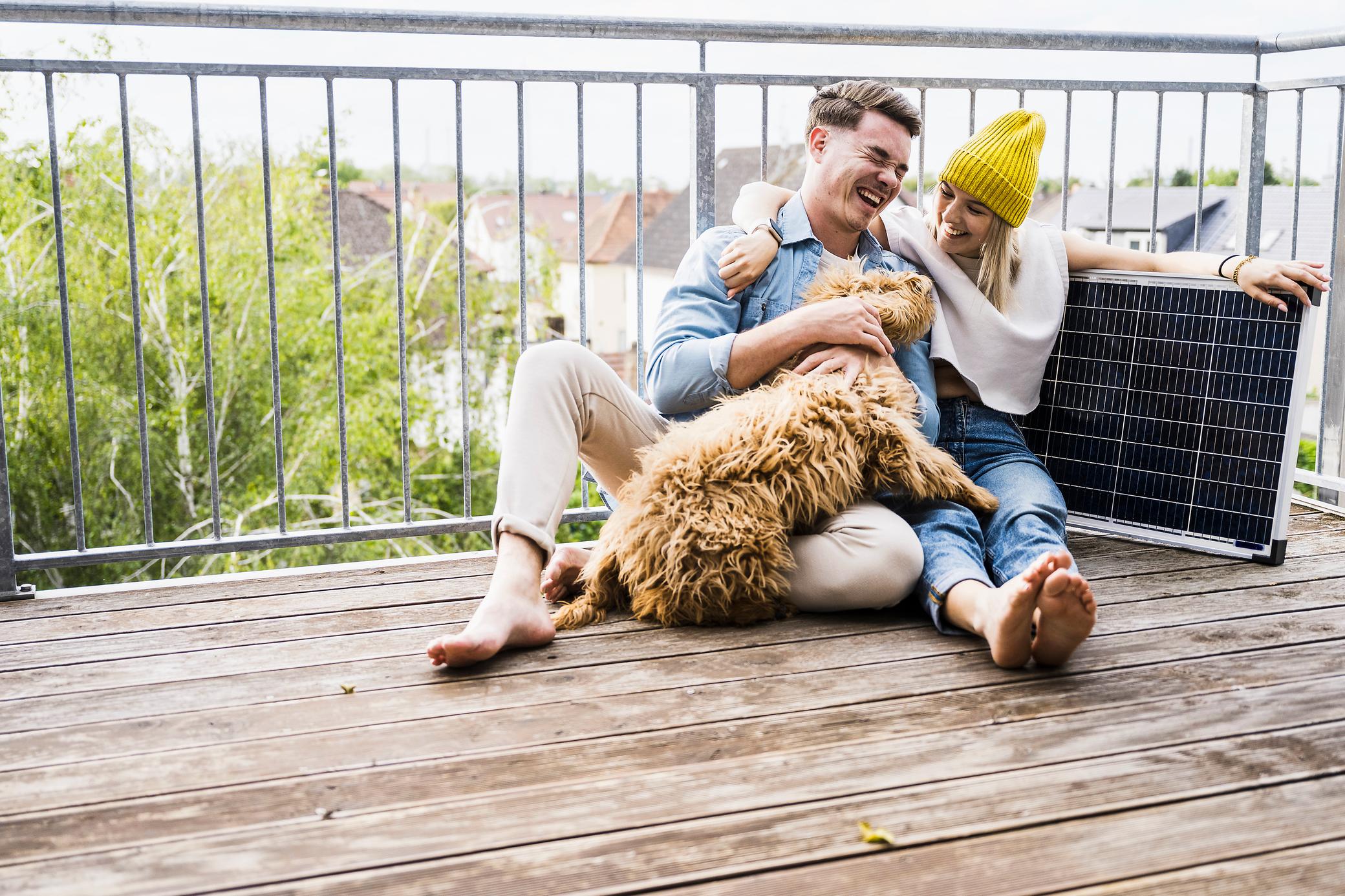 Mann und Frau auf Balkon mit Hund und Solarpanel.