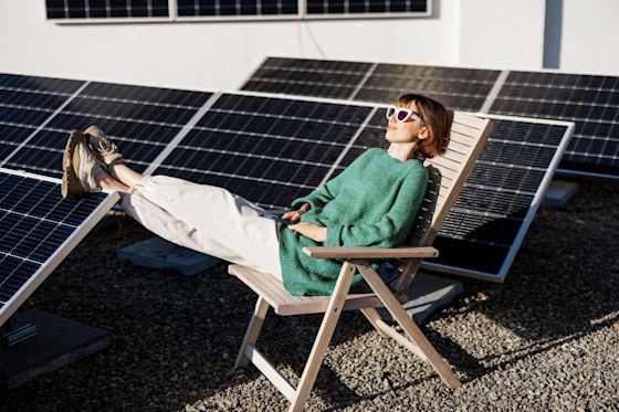 Solaranlagen gibt es auch für dein Flachdach Junge Frau sitzt entspannt auf einem Liegestuhl und ruht sich auf einem Flachdach mit Solaranlage aus.