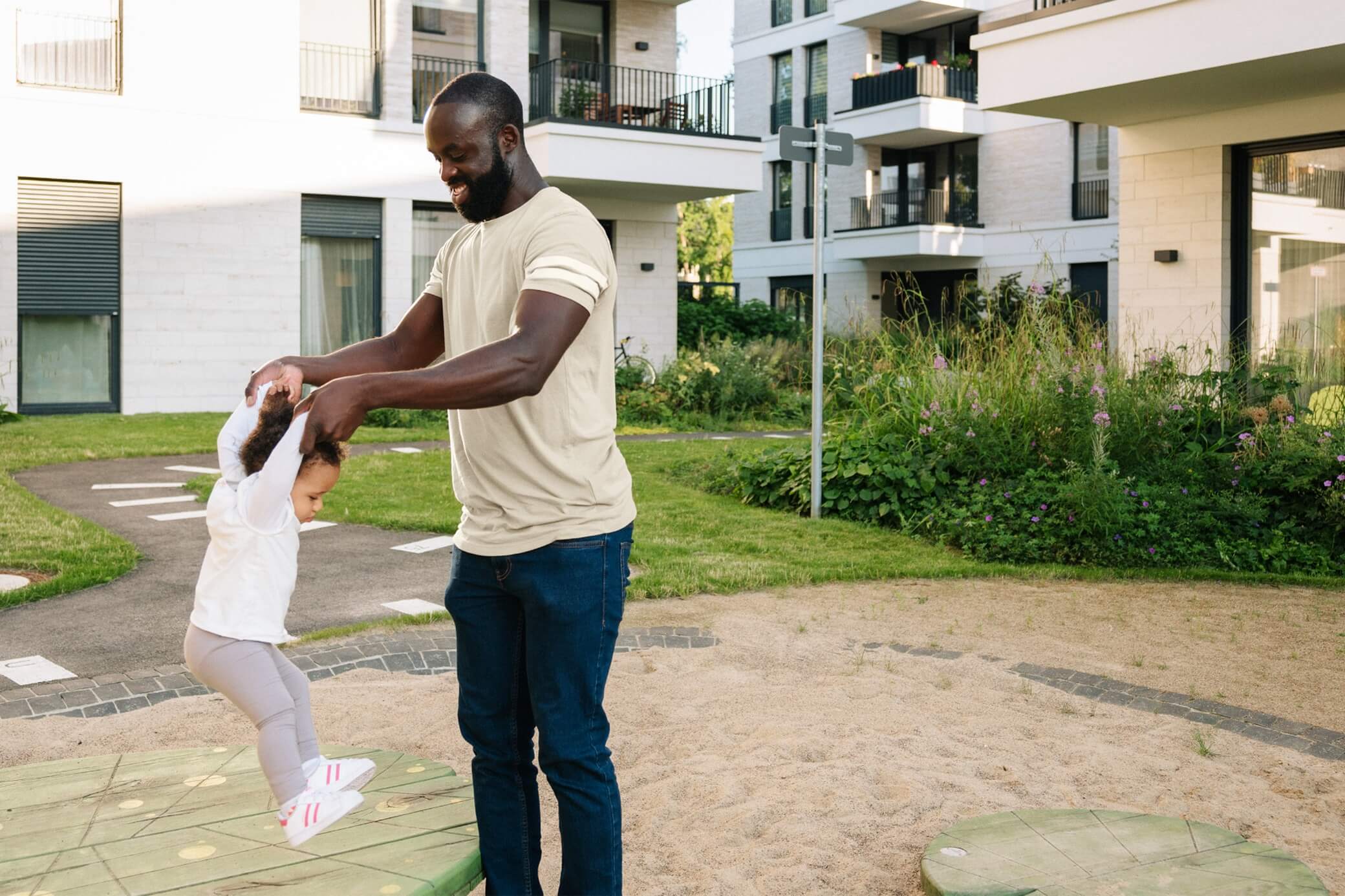 Im Mehrfamilienhaus werden viele CO2-Emissionen verursacht Mann spielt mit Kleinkind auf einem Spielplatz im Mehrfamilienhaus