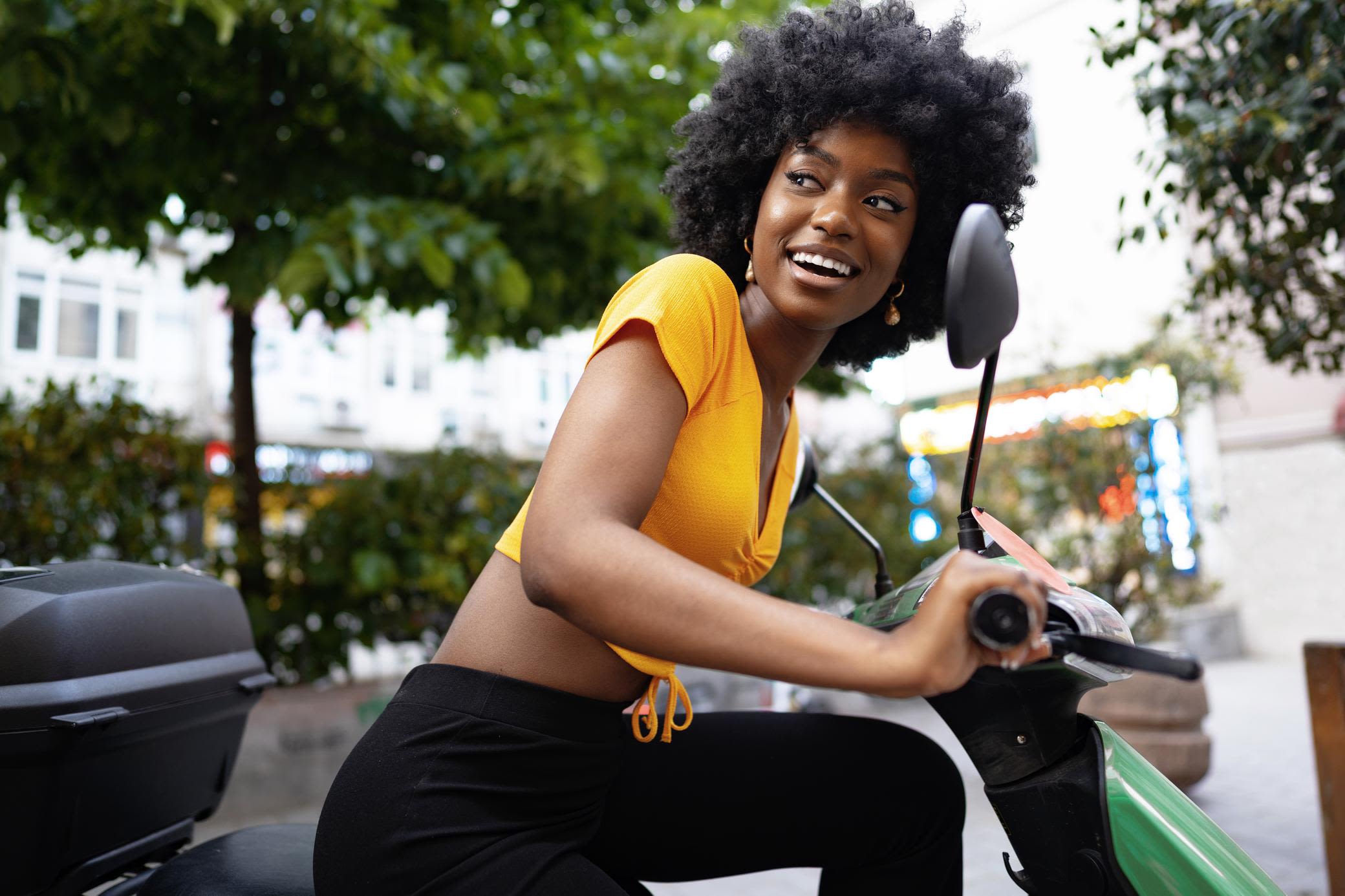 Mit dem E-Roller geht es leise durch die Stadt Frau im gelben Shirt fährt auf E-Roller durch die Stadt