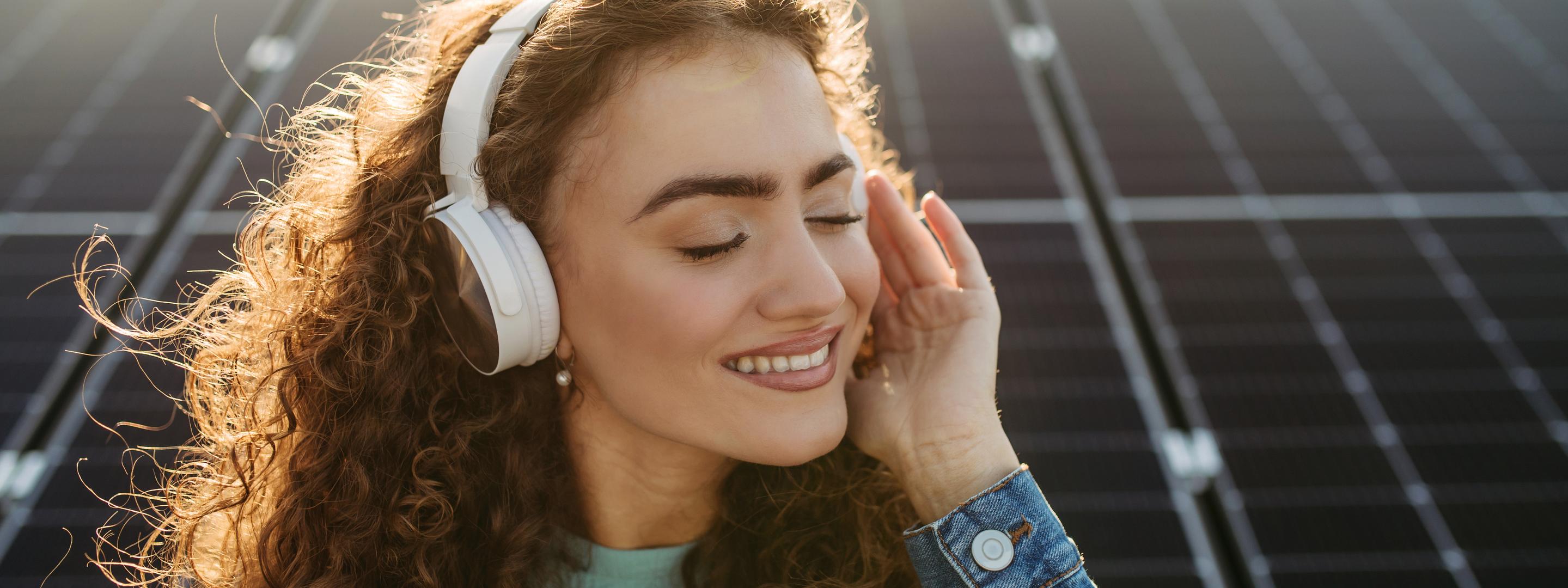 Frau mit Kopfhörern hört Musik vor Solaranlage