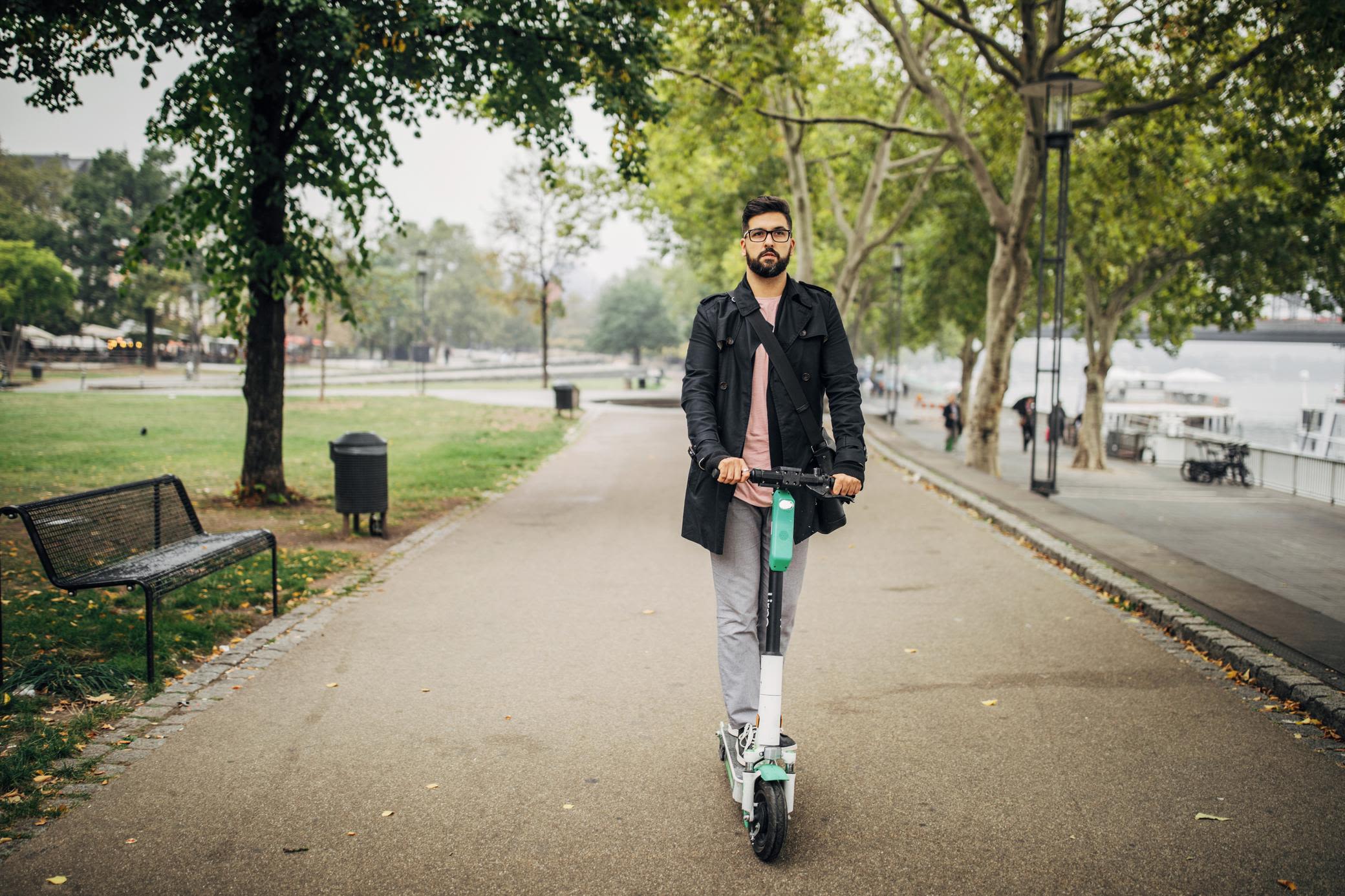 Mit refurbished E-Scooter bis du günstig unterwegs Mann mit E-Scooter fährt durch den Stadtpark.