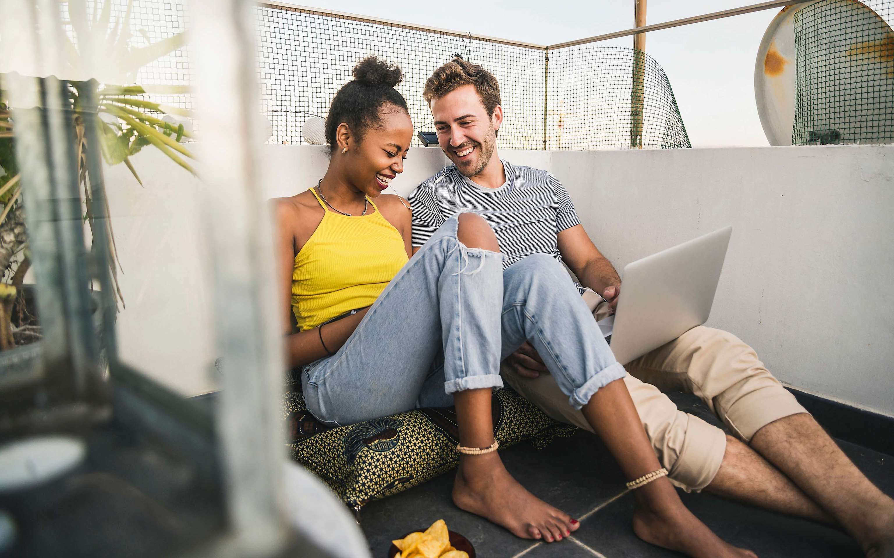 Bleib flexibel und wechsel deinen Stromanbieter zu Yello Junges, fröhliches Paar mit Laptop sitzt auf dem Balkon