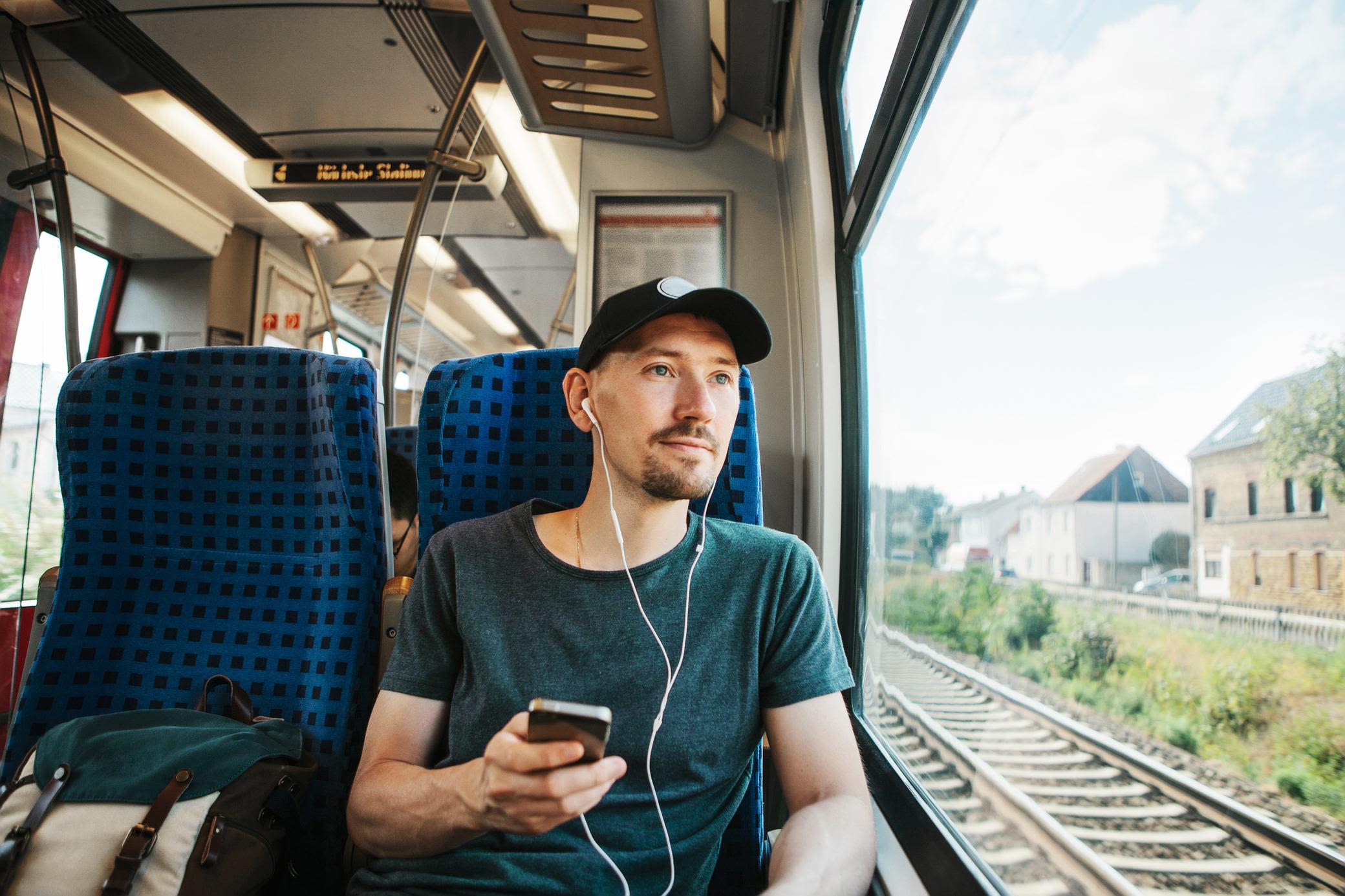 Mit nachhaltiger Mobilität kannst du CO2 und Kosten sparen Junger Mann mit Kappy und Handy fährt im Zug
