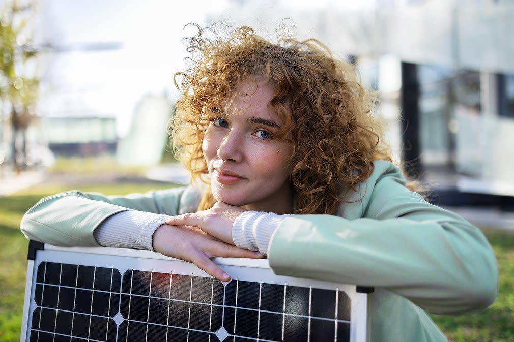 Das richtige Photovoltaik-Komplettpaket finden und unabhängig werden - so easy. Frau mit Locken lehnt auf einem Solarmodul im Garten