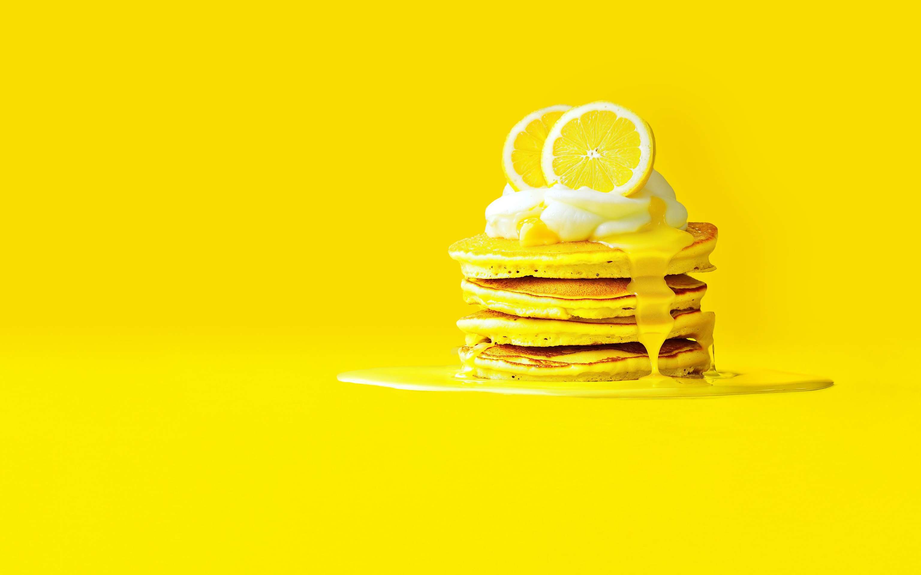 Zitronen mixen? Mix lieber unsere Energietarife von Yello Pfannkuchenstapel mit Zitronenscheiben und weißer Soße auf gelbem Untergrund - KI generiert