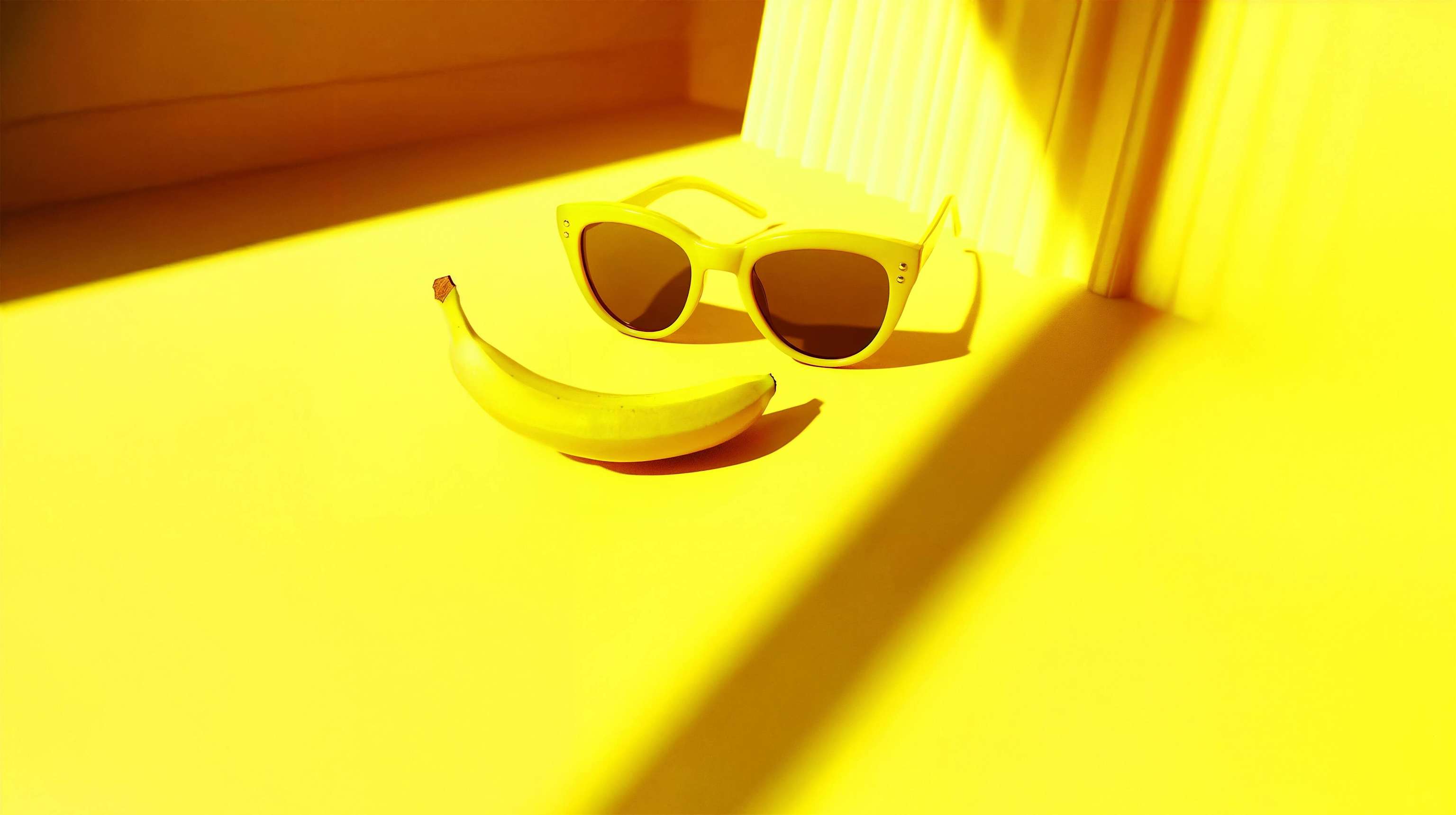 Gelbe Sonnenbrille und Banane liegen auf gelbem Untergrund. Gelbe Sonnenbrille und Banane liegen auf gelbem Untergrund.