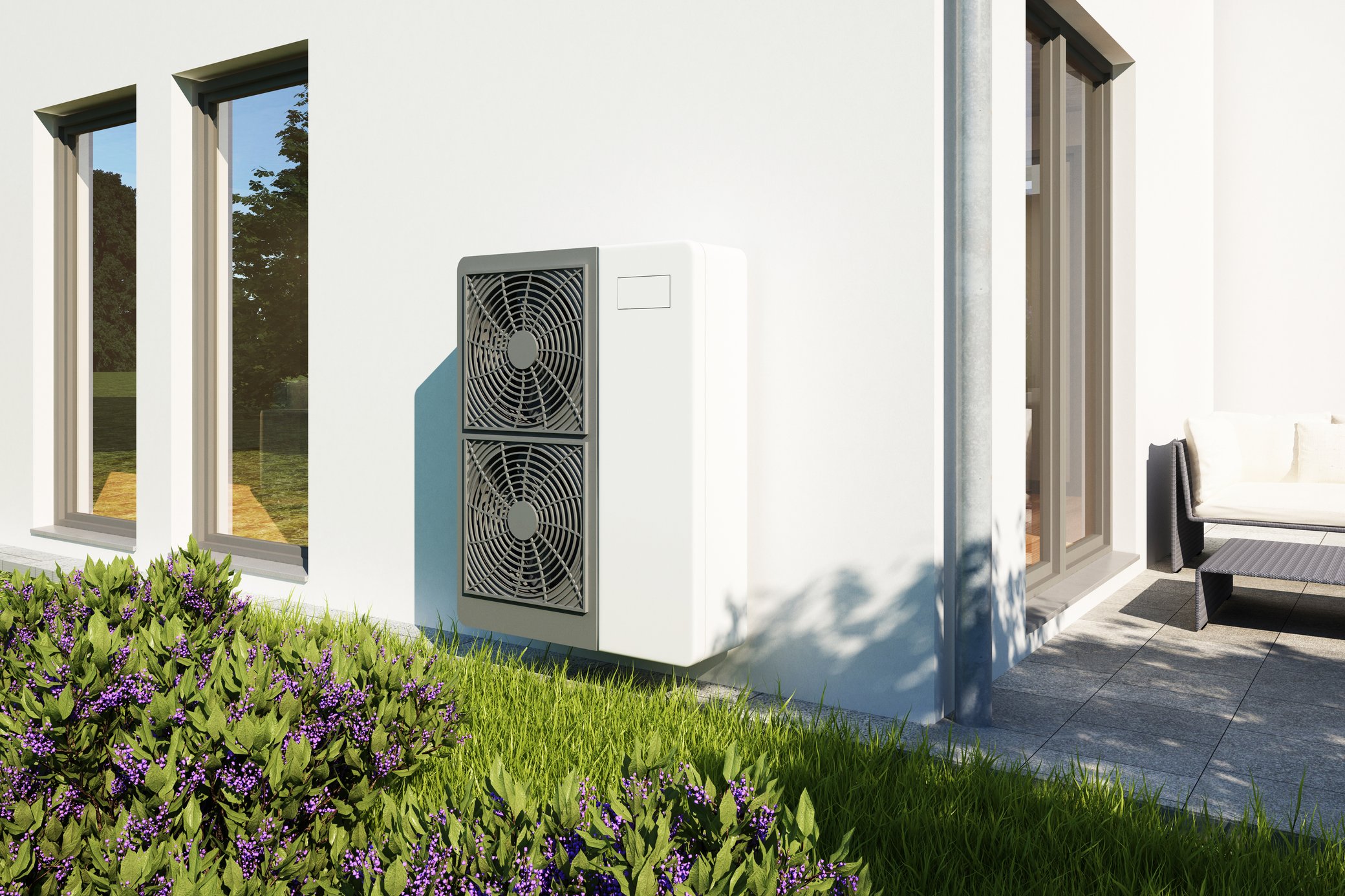 Eine Wärmepumpe steht vor heller Hauswand im Garten
