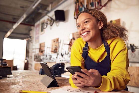 Gute Energie für dein Gewerbe einfach zu fairen Preisen beziehen Frau mit einem Handy in der Hand arbeitet in einer Werkstatt