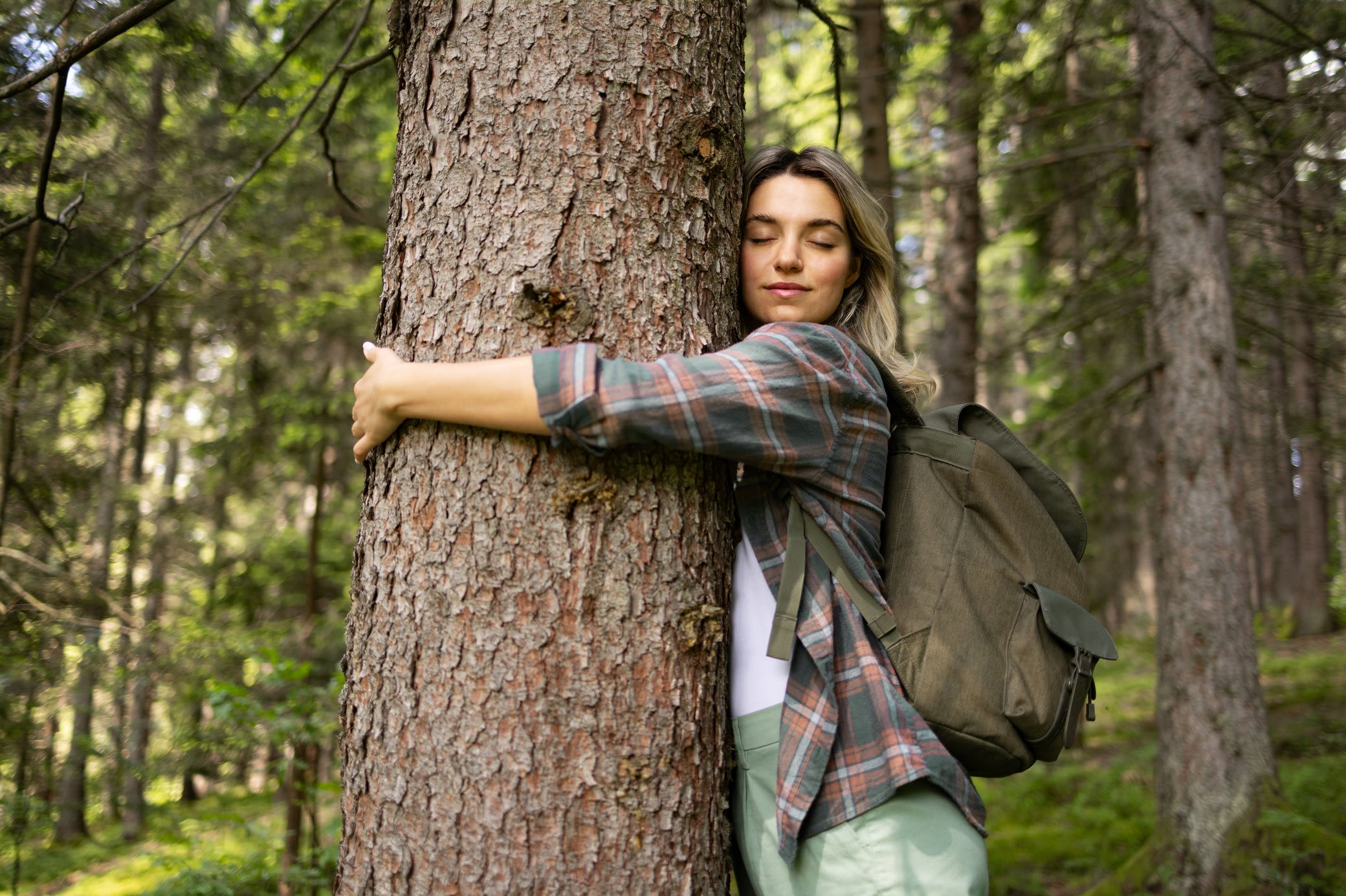 Naturschutz sind uns bei Yello ein Anliegen Frau umarmt mit geschlossenen Augen einen Baum in einem Wald