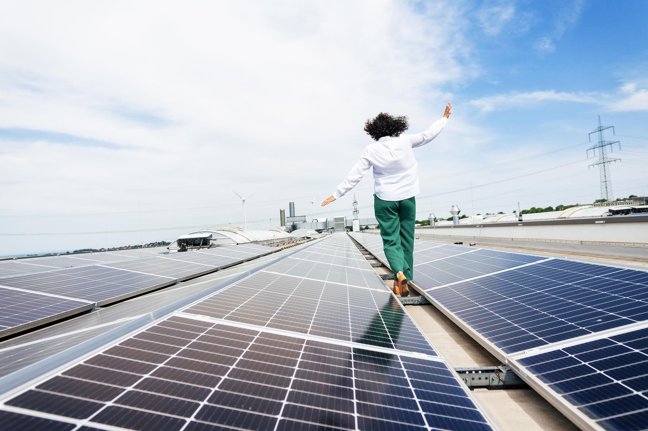 Eine eigene Solaranlage bringt grünen Strom aufs Dach Frau balanciert barfuß auf einem Flachdach mit Solaranlage