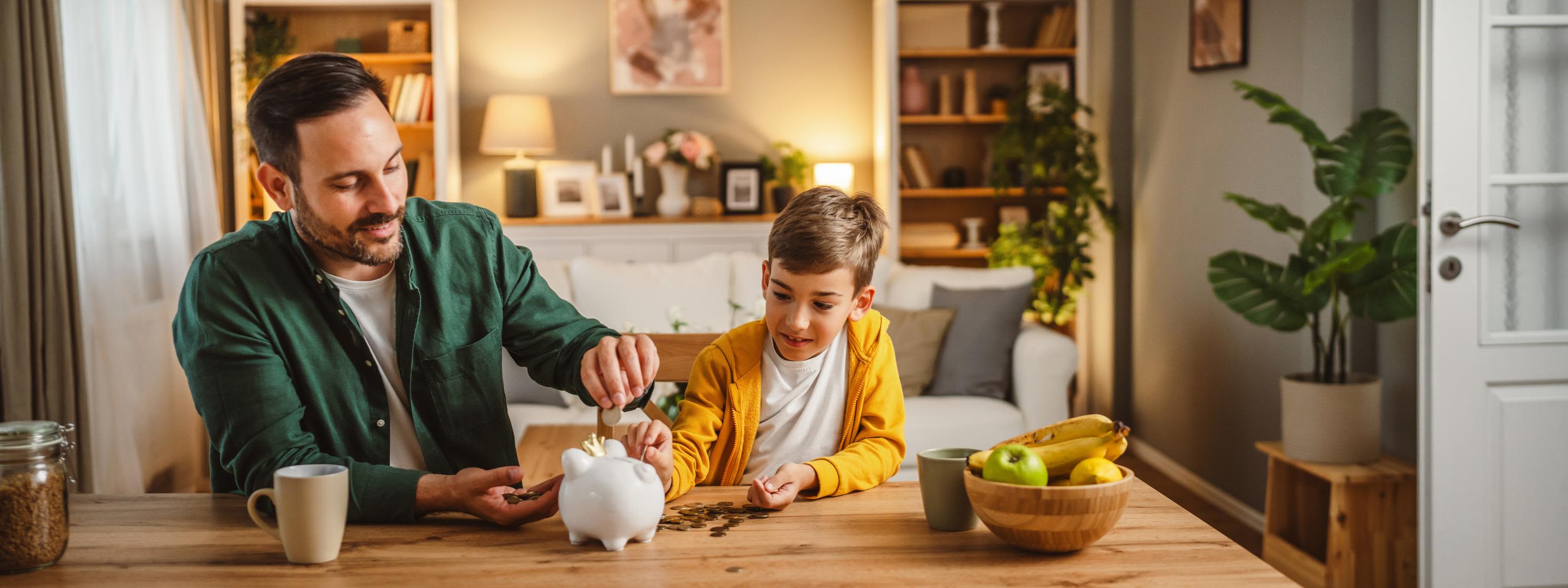 Die Energiepreisbremse hat dich vor zu hohen Kosten geschützt Vater und Sohn sitzen am Tisch im Wohnzimmer und füllen Sparschwein auf