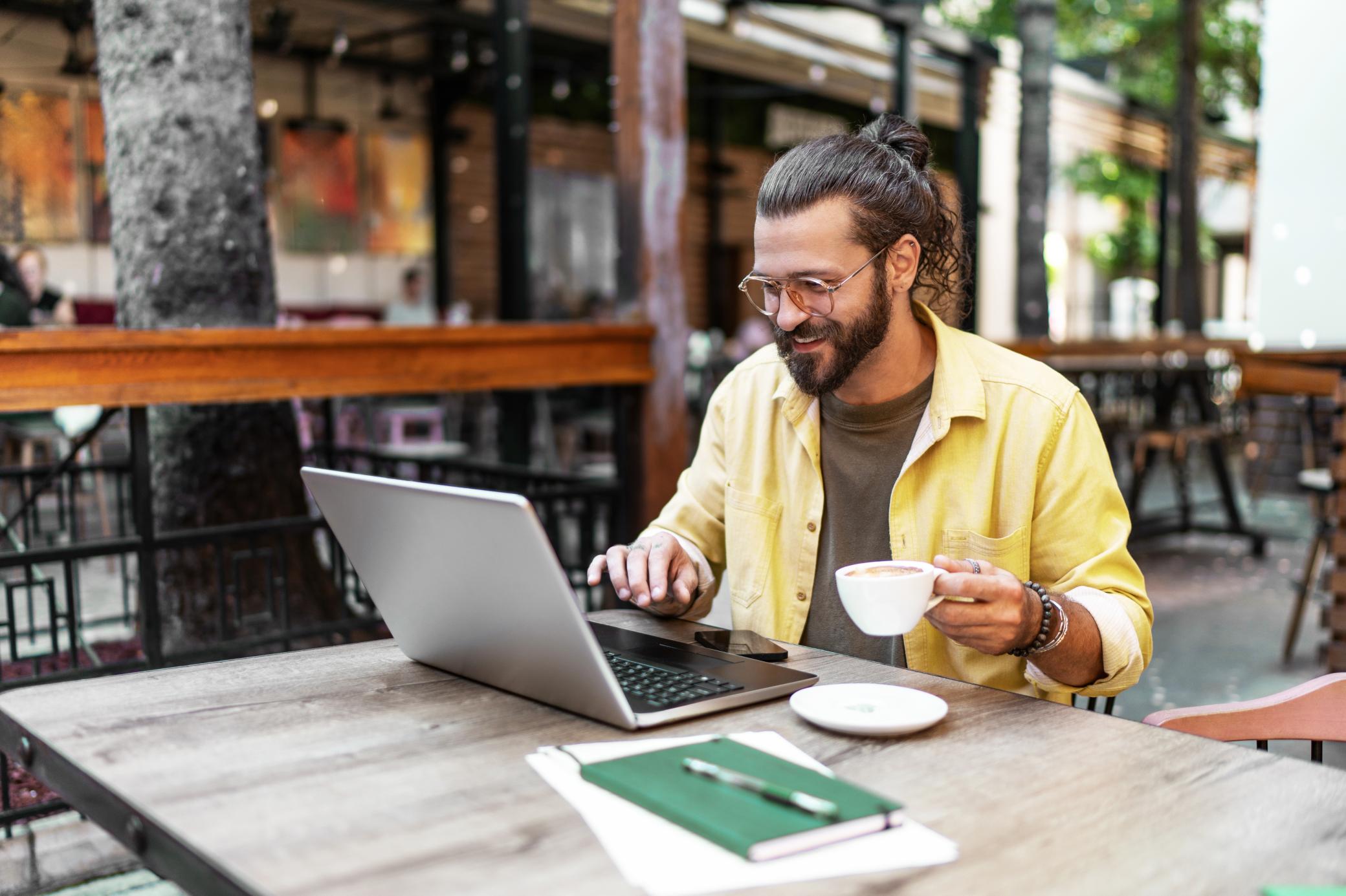 Junger Mann arbeitet in einem Café während sein E-Auto lädt
