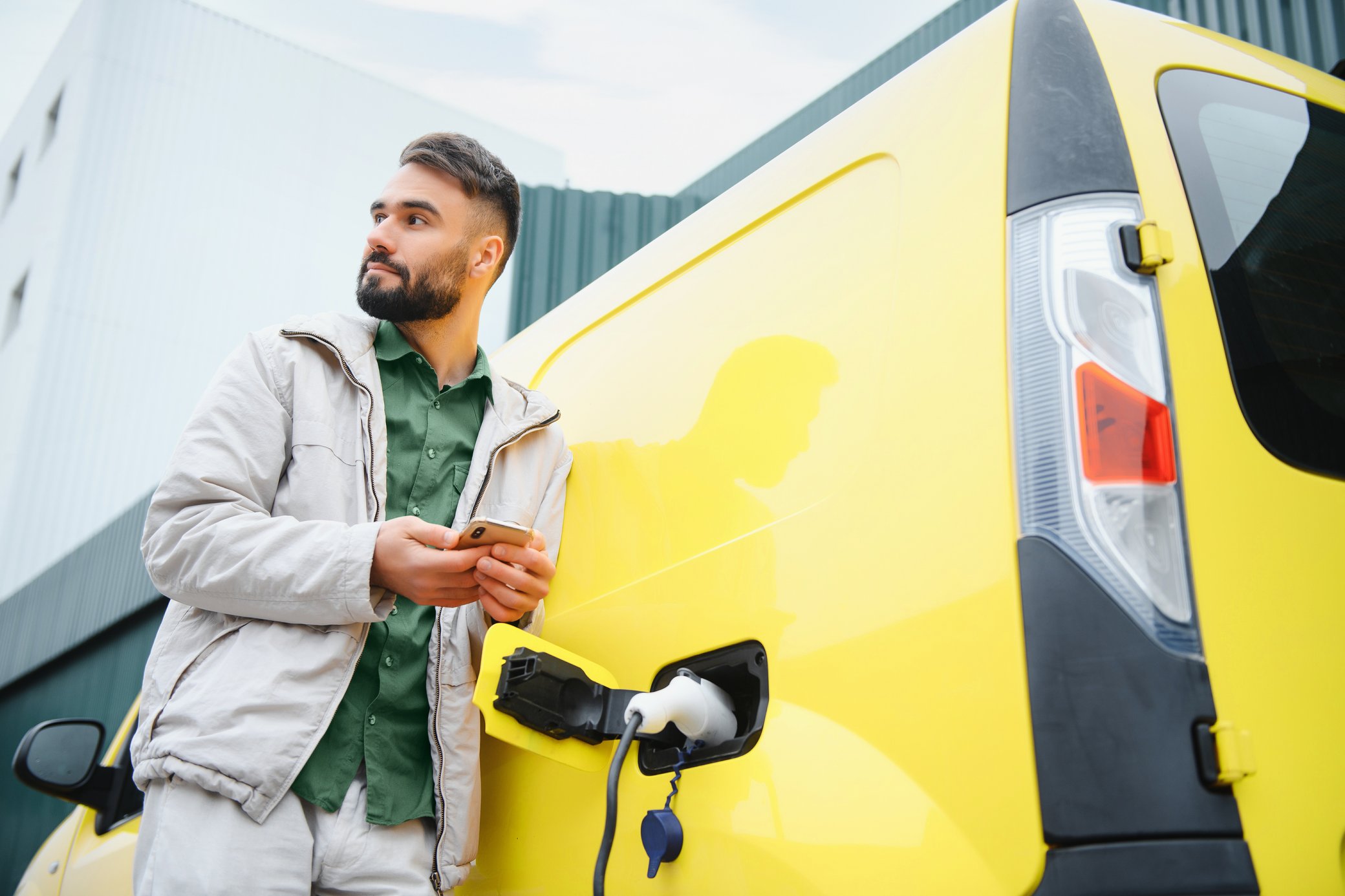 Ein Mann mit Handy in der Hand lädt seinen elektrischen Minivan