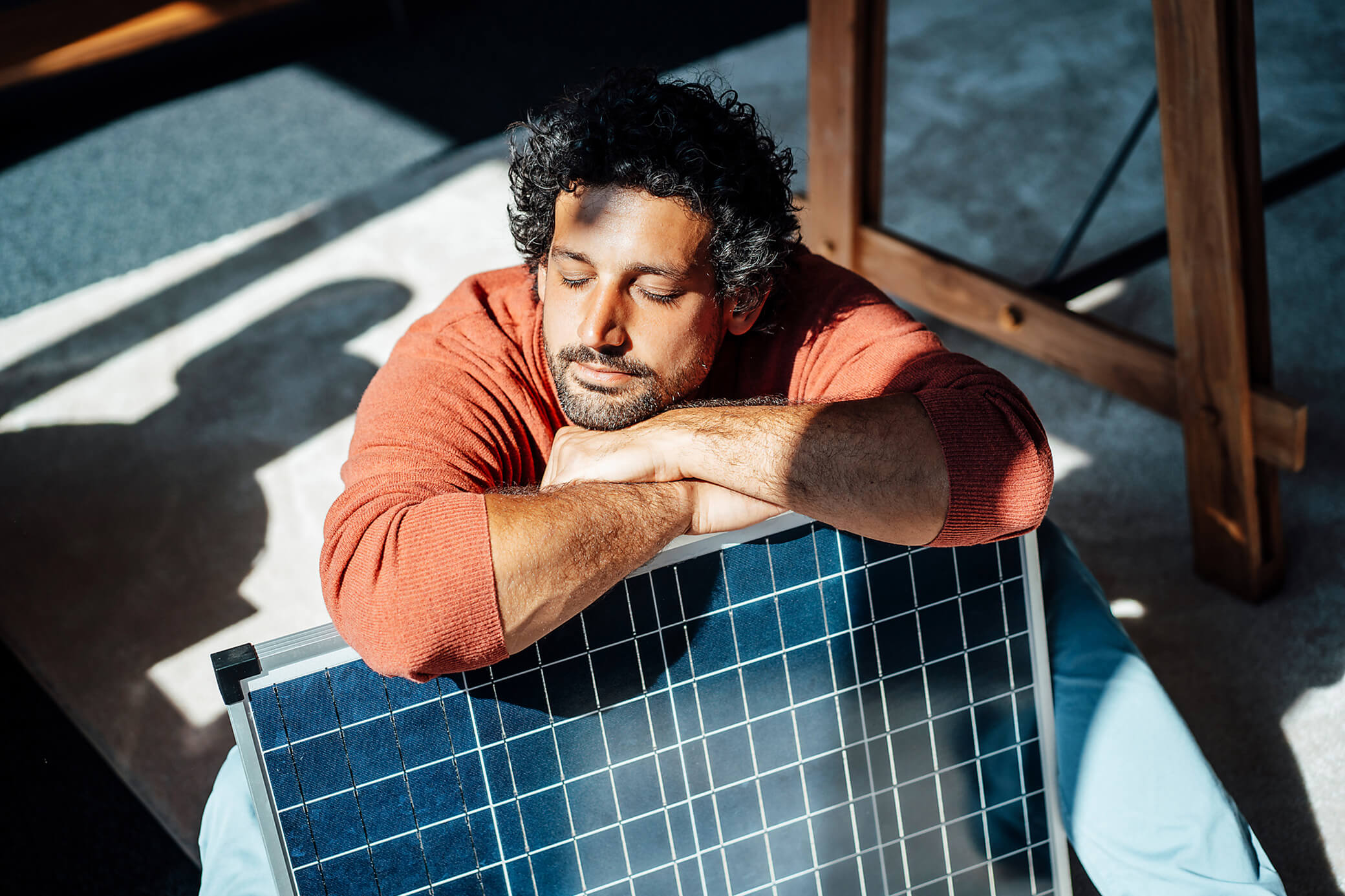 Mann mit orangem Pullover lehnt entspannt auf einem Solarmodul