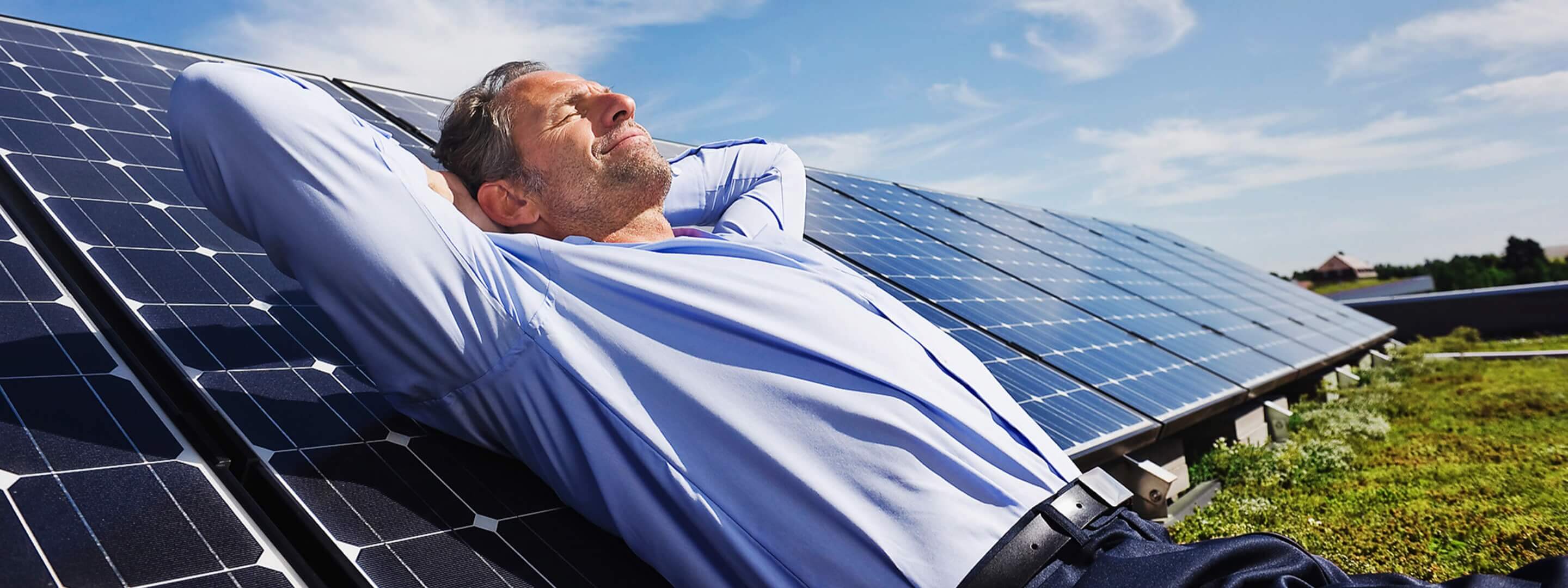 Mit Photovoltaik im Komplettpaket entspannt zum grünen Strom Mann liegt auf einer Photovoltaikanlage und sonnt sich.