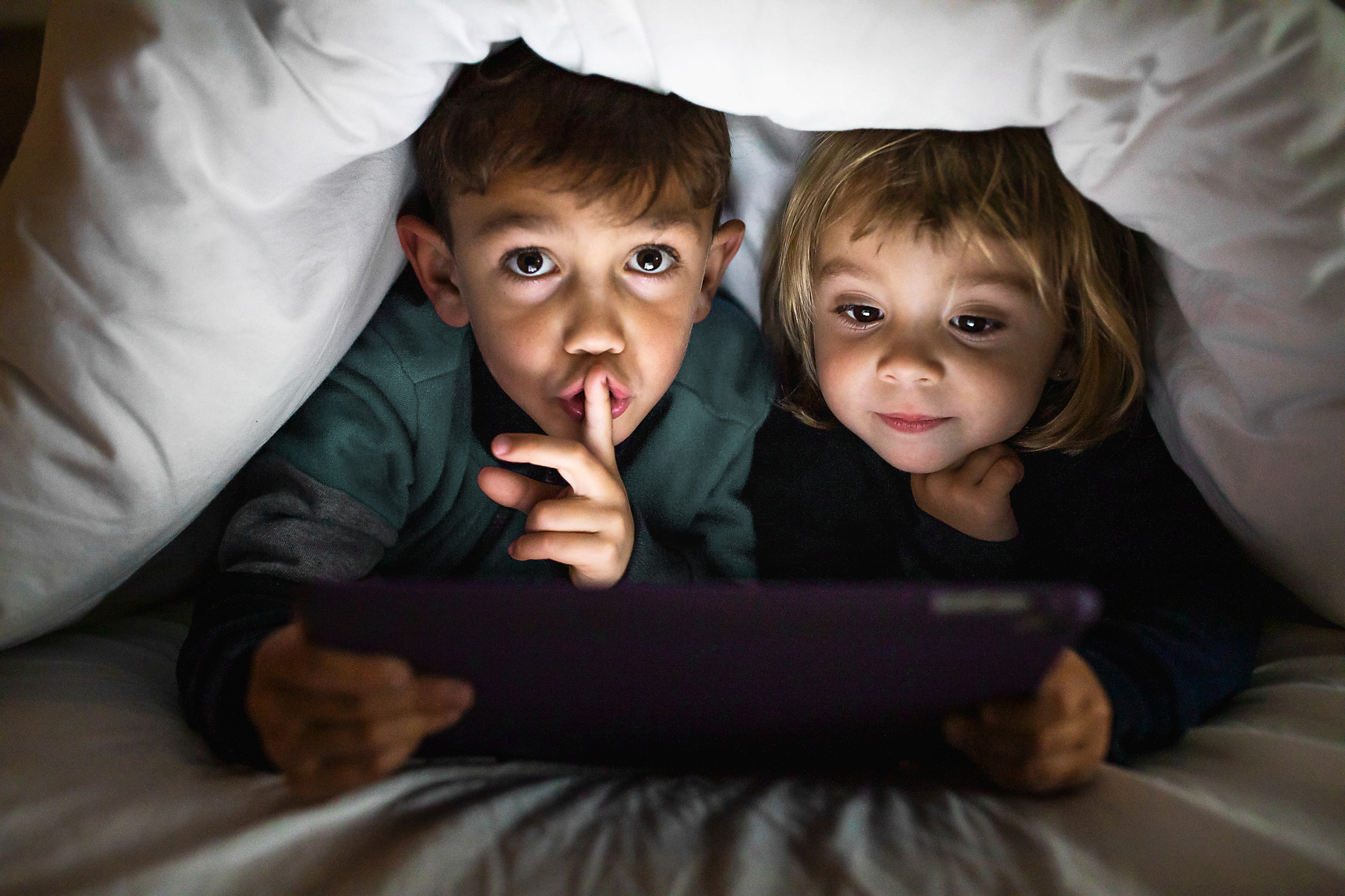 Geschwister schauen auf Tablet unter einer Decke