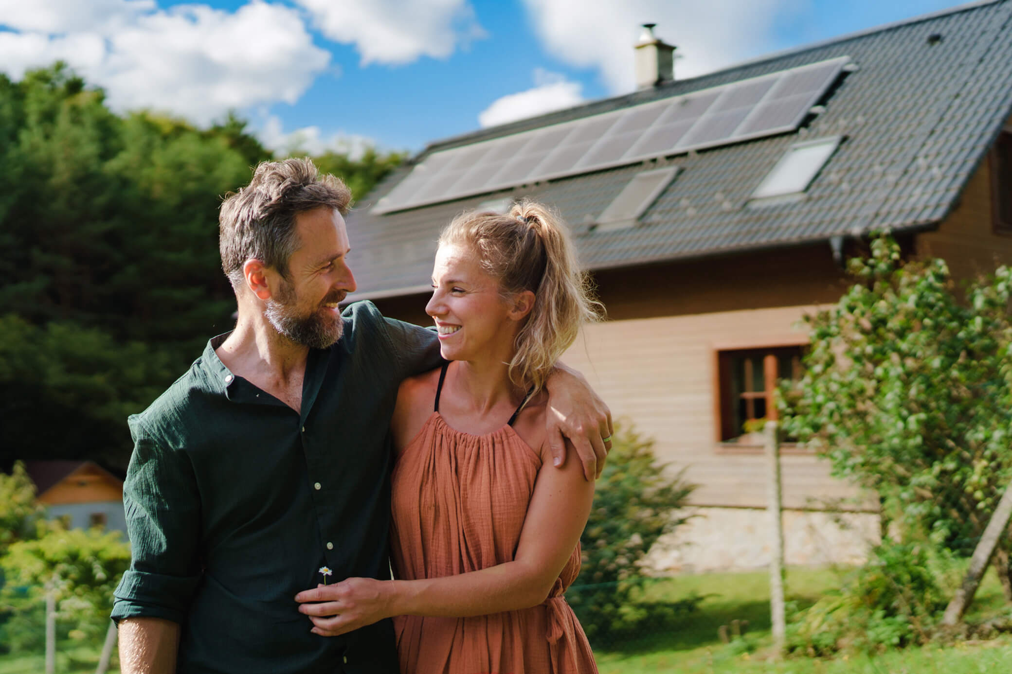 Frau und Mann stehen Arm in Arm vor Haus mit Solaranlage