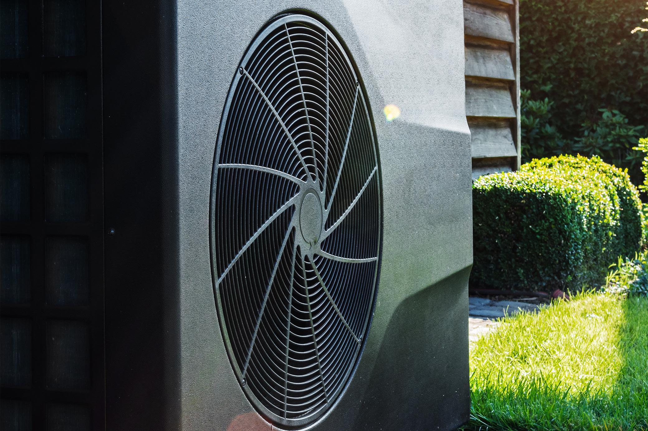 Mit einer Wärmepumpe heizt du dein Zuhause energieeffizient Schwarze Wärmepumpe hinterm Haus im Garten