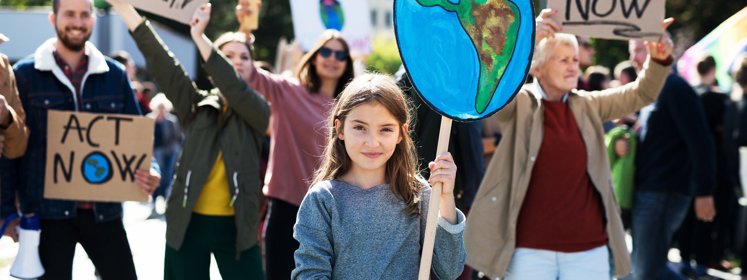 Mädchen hält auf einer Demo lächelnd ein Plakat mit gemalter Erdkugel hoch.