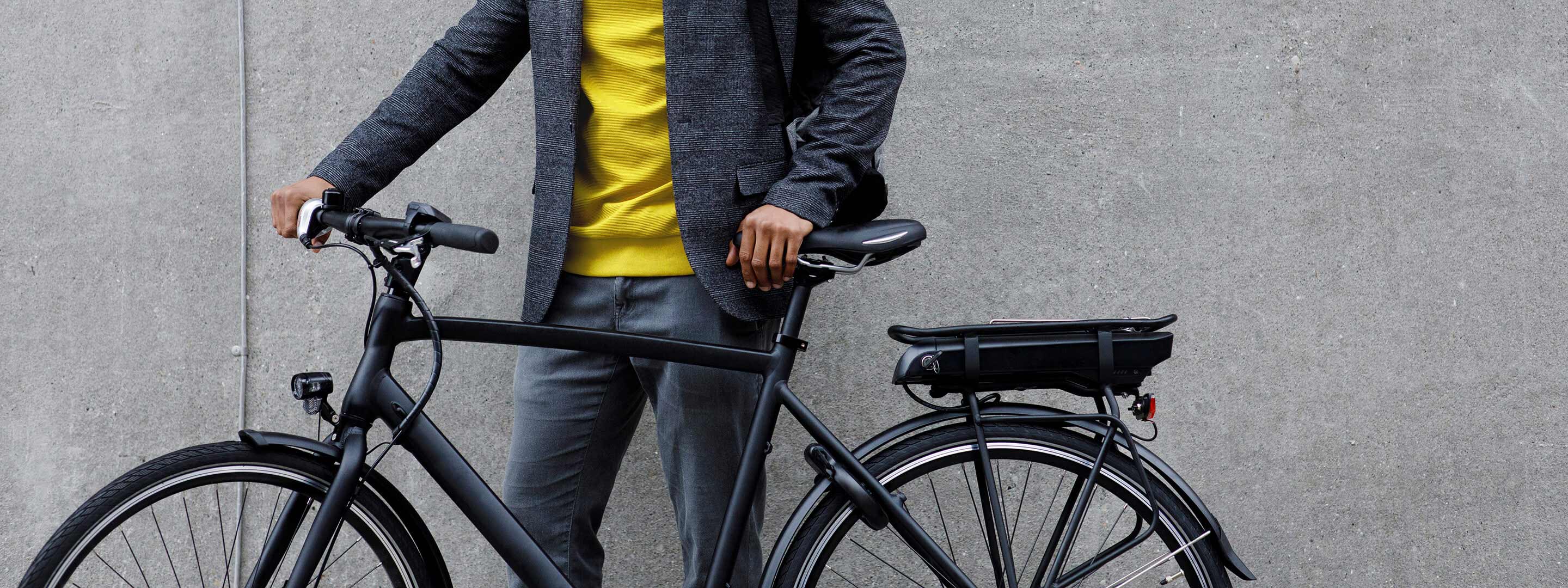 Mann steht mit seinem E-Bike Fahrrad vor einer grauen Wand