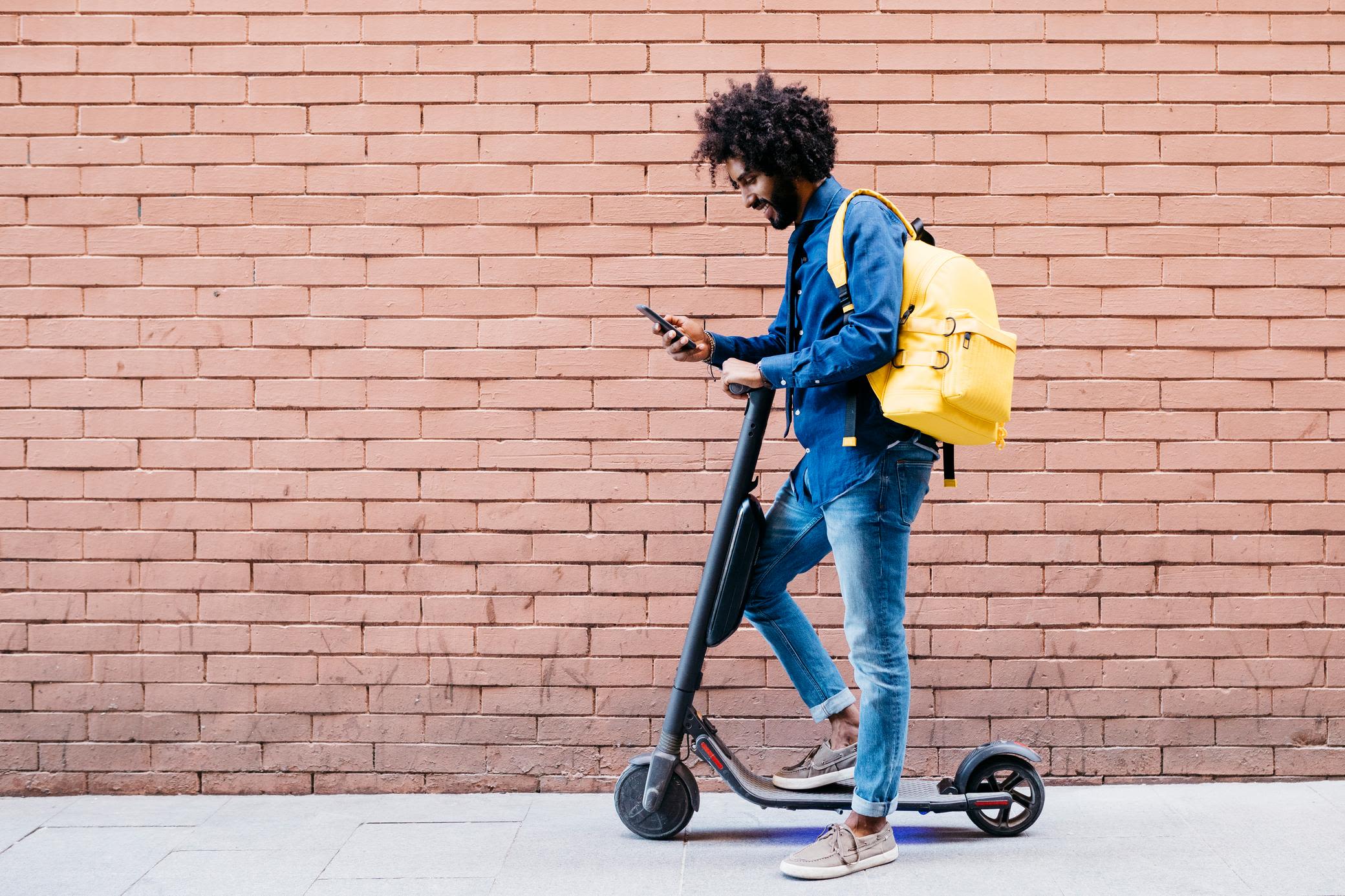 Vor dem E-Scooter Kauf zählt richtig informieren Mann mit E-Scooter schaut aufs Smartphone