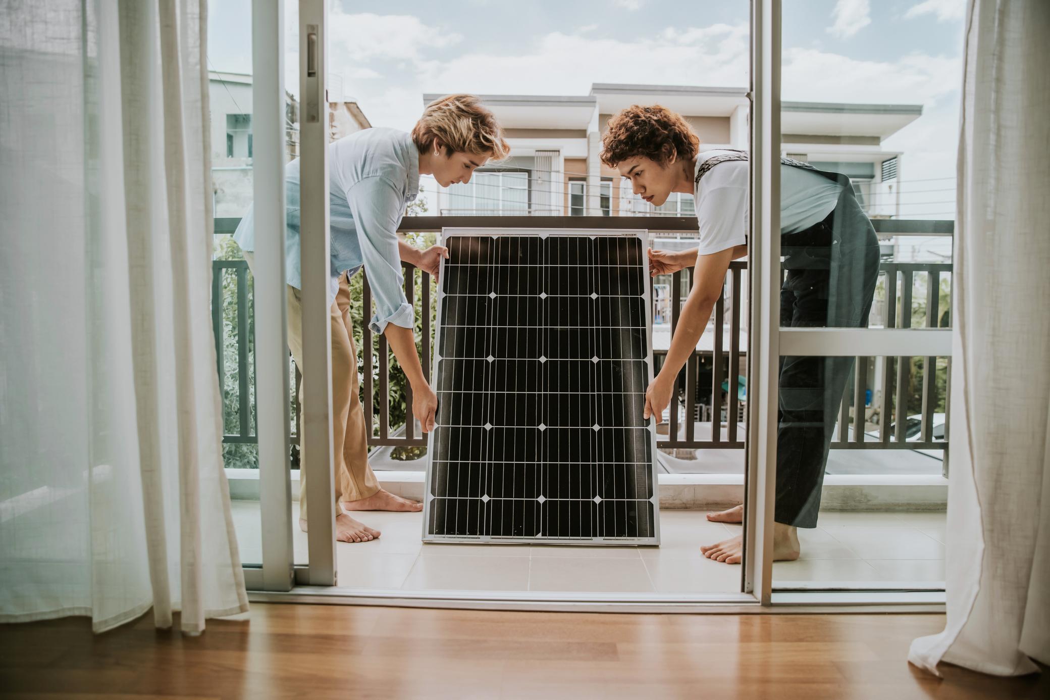 Zwei junge Frauen installieren ein Solarmodul auf dem Balkon