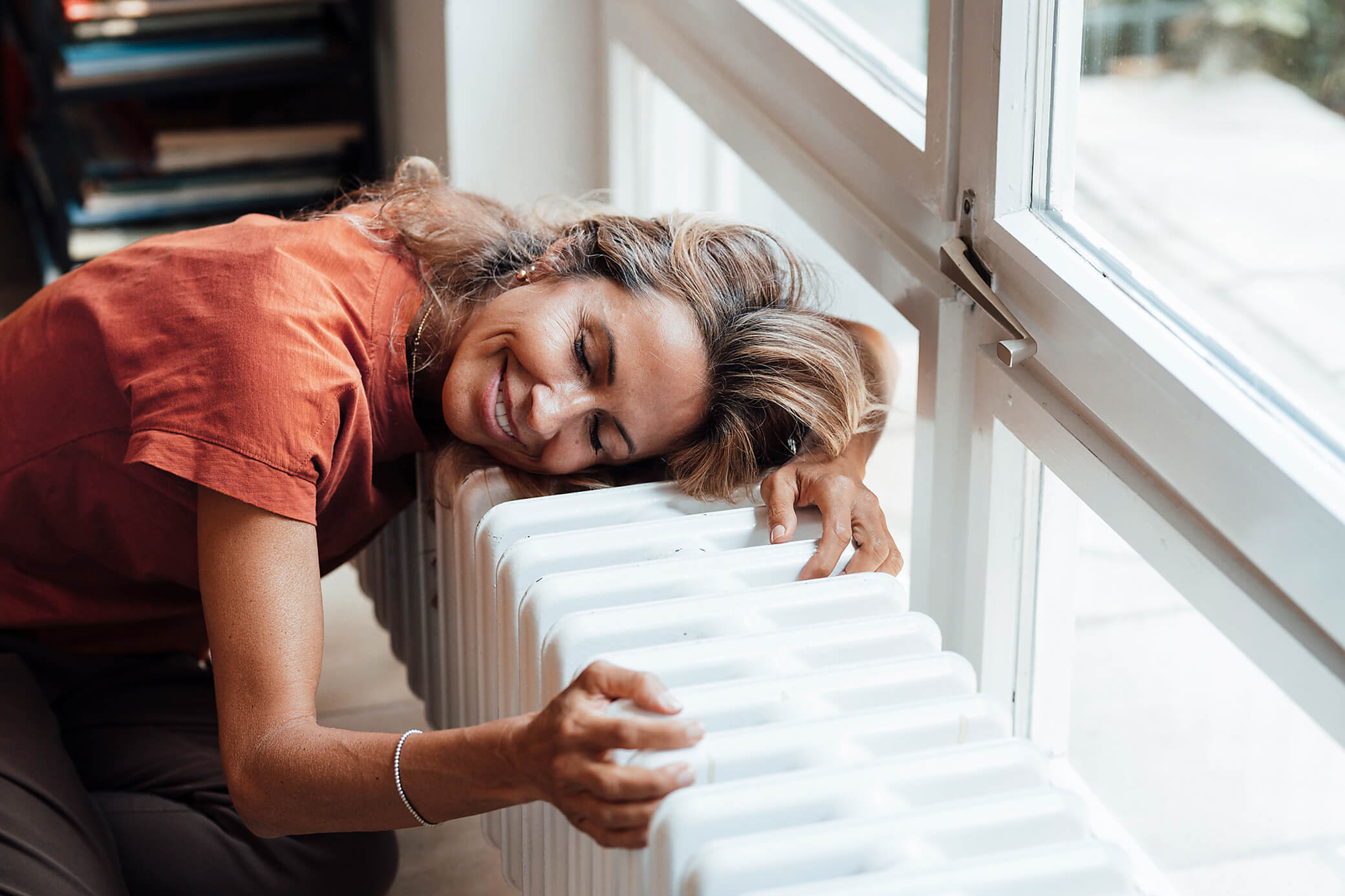 Heiz dein Zuhause mit Energie aus der Umwelt Frau am Fenster schmiegt sich an einen Heizkörper