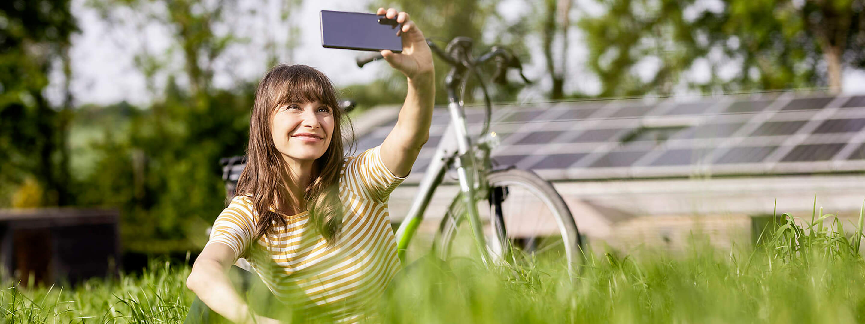 Eine Frau mit Fahrrad macht ein Selfie vor ihrer Photovoltaikanlage.