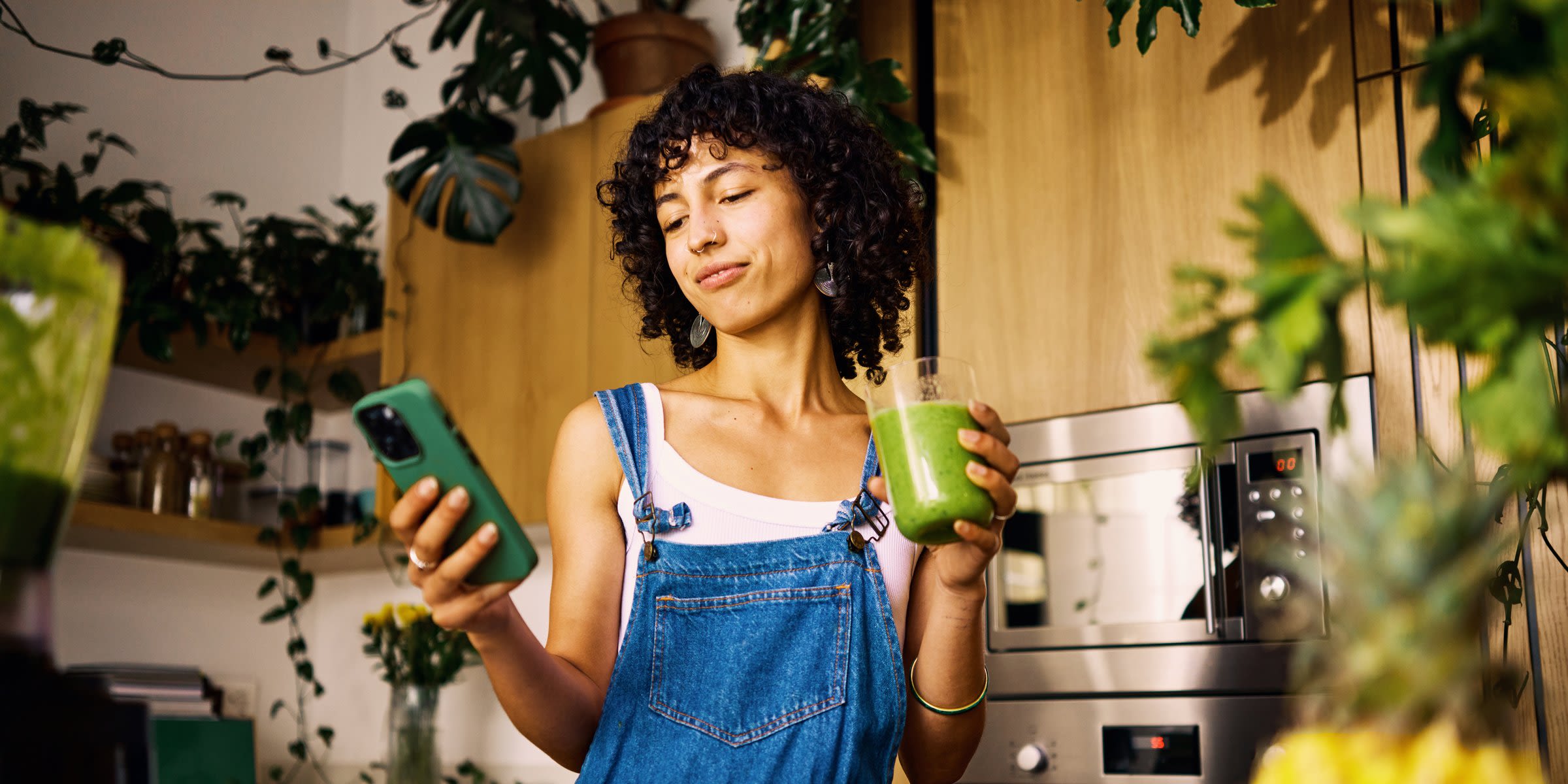 Mach dir deinen eigenen Strommix - am besten grün Frau mit Smoothie in der Hand steht in der Küche und schaut auf ihr Smartphone