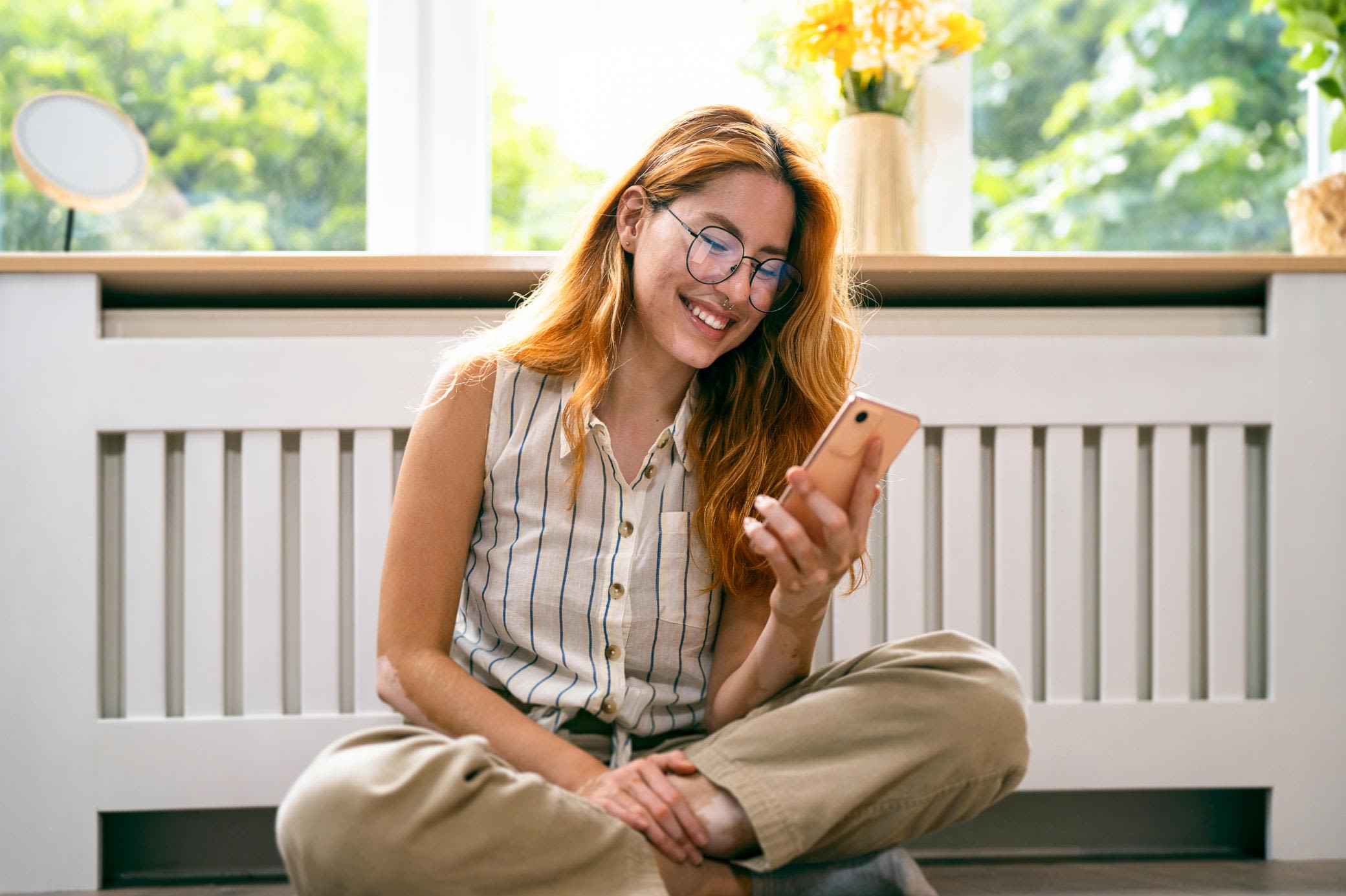 Beim Heizen sparen: mit Energie aus Solarthermie und passenden Tarifen Frau sitzt vor ihrer Heizung und schaut auf ihr Smartphone.