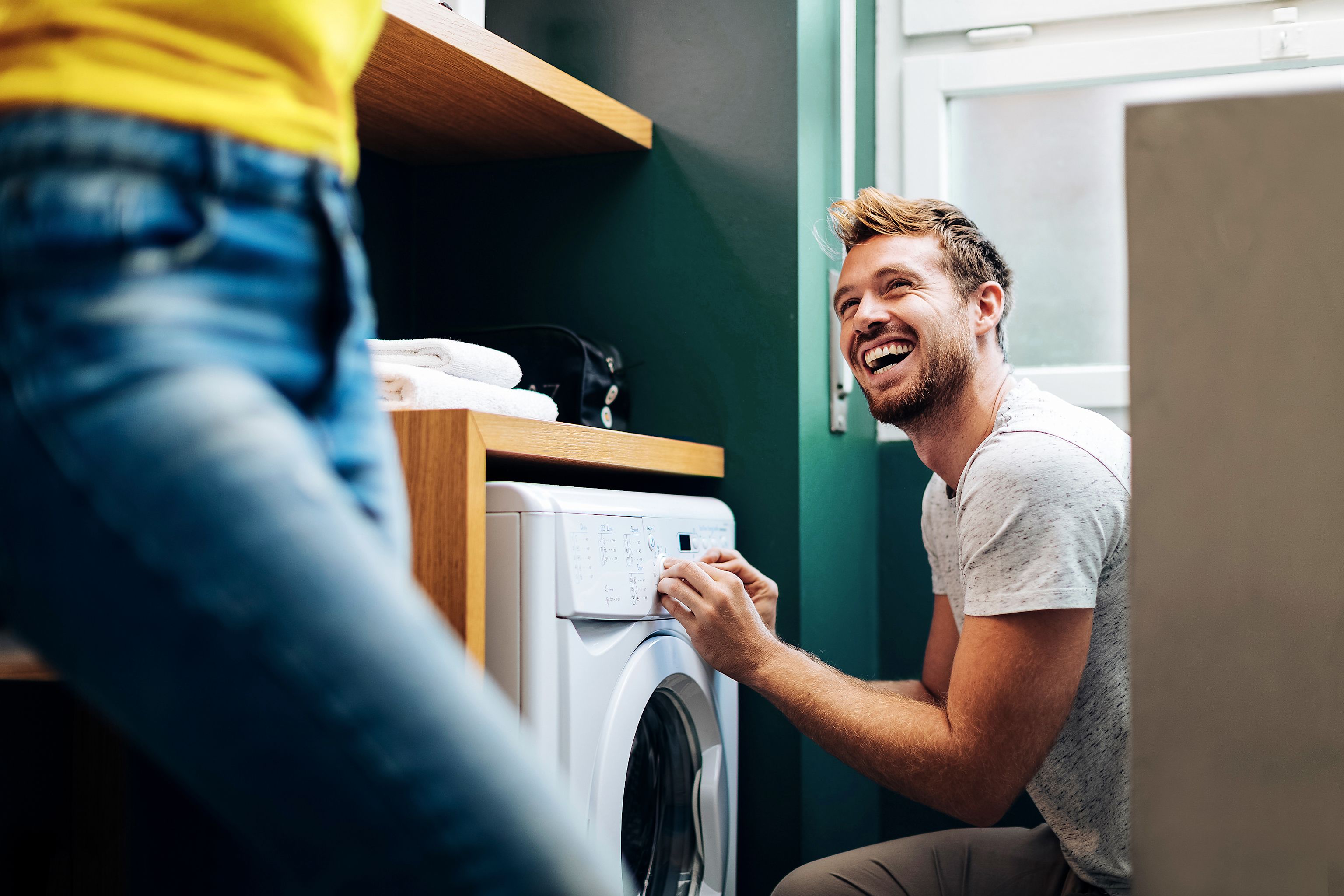 Flexibel und smart: Die neuen Stromtarife von Yello. Ein glücklicher junger Mann, der seine Freundin ansieht und die Wäsche zu Hause wäscht.