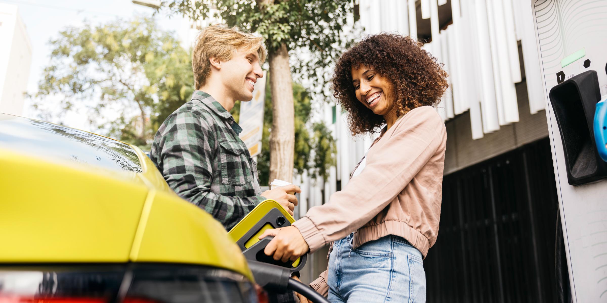 Junges Paar lädt lachend ihr gelbes E-Auto in der Stadt auf