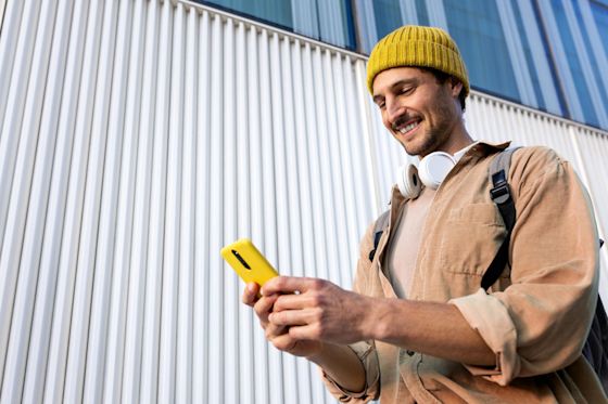 Die Wallbox kann man Zuhause vor Stromklau schützen beispielsweise mit RFID Sicherung Mann mit gelber Mütze und Kopfköhrern schaut auf ein gelbes Handy in seinen Händen