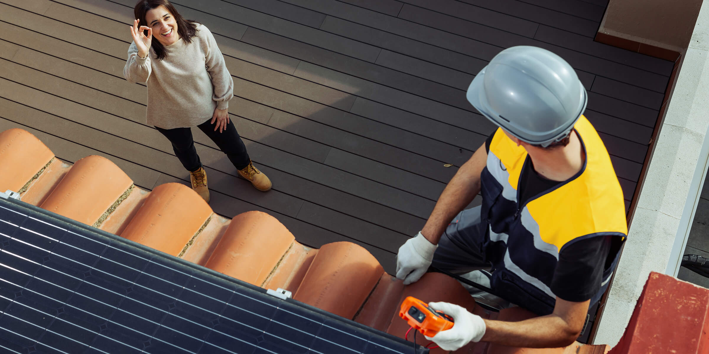 Techniker installiert Solaranlage auf dem Dach, die Kundin ist zufrieden.