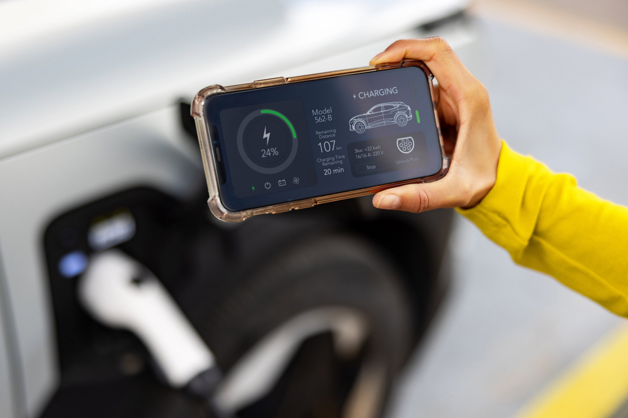 Eine Person hält ein Smartphone mit App zur Überwachung des Ladevorgangs eines Elektroautos