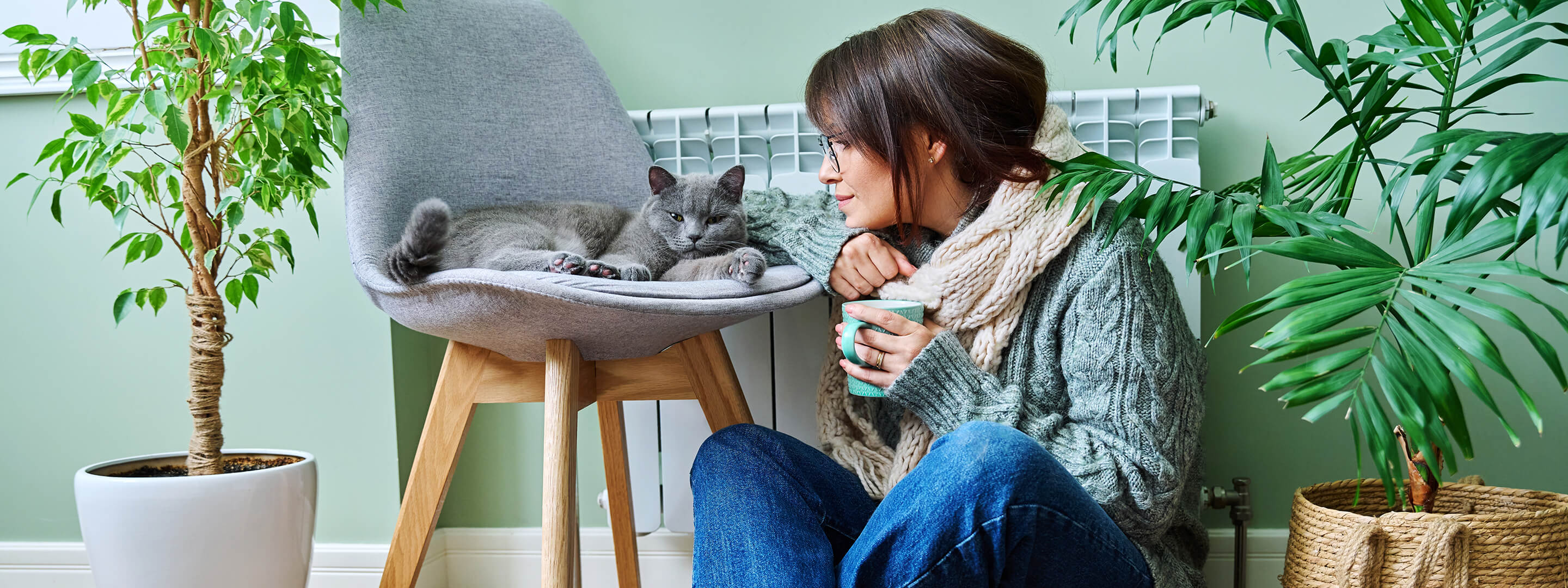 Frau sitzt in warmer Kleidung mit Katze vor der Heizung