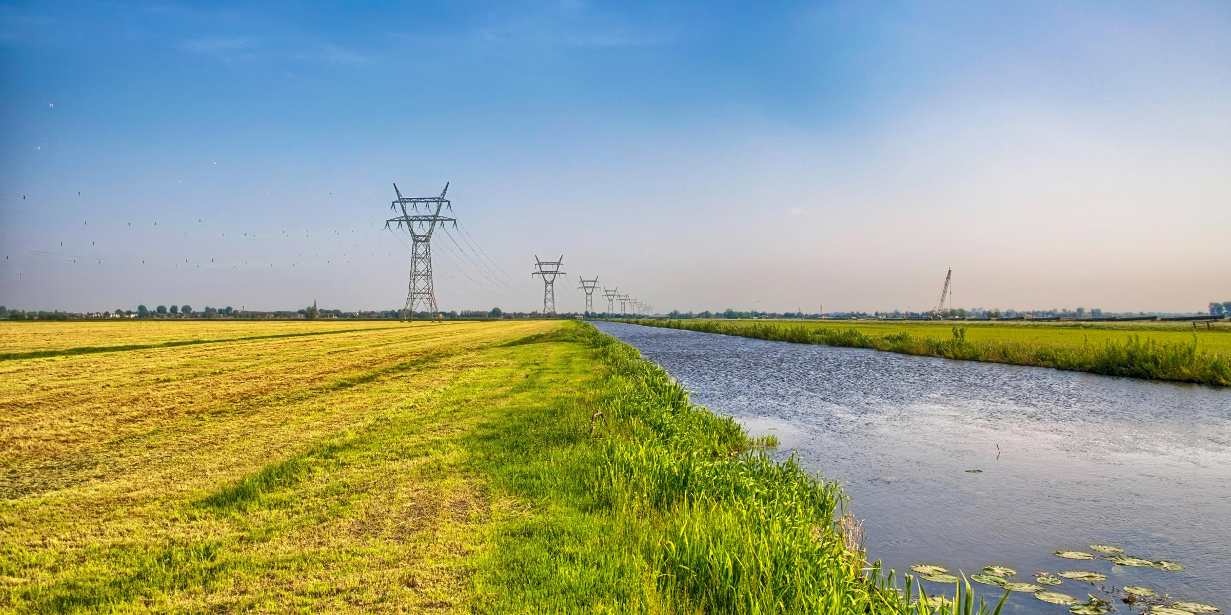 Hochspannungsleitungen und Strommasten auf einem Feld an einem Kanal