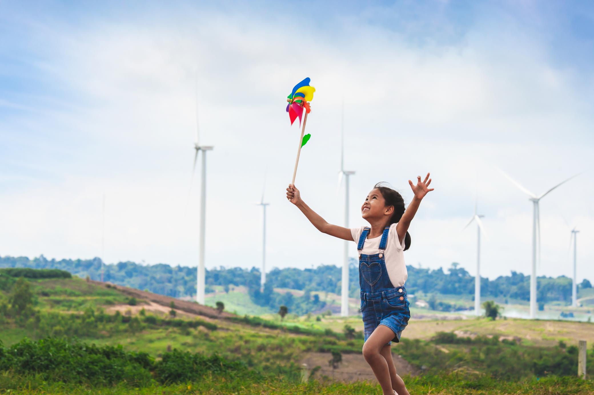 Mädchen läuft mit buntem Windrad durch einen Windpark