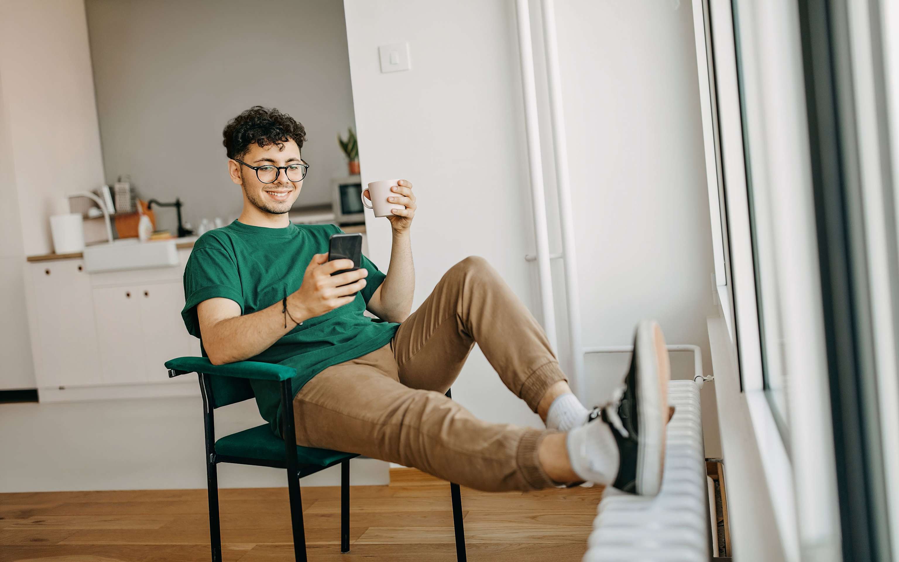 Einfach verstehen: Deine Yello Energie-Rechnung Mann schaut auf sein Handy und legt die Füße auf die Heizung