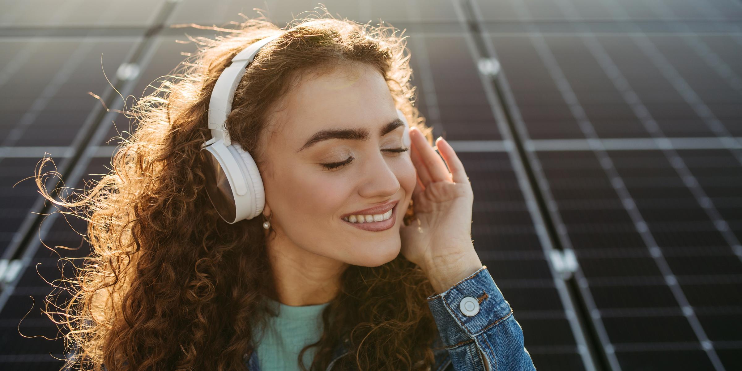 Frau mit Kopfhörern hört Musik vor Solaranlage