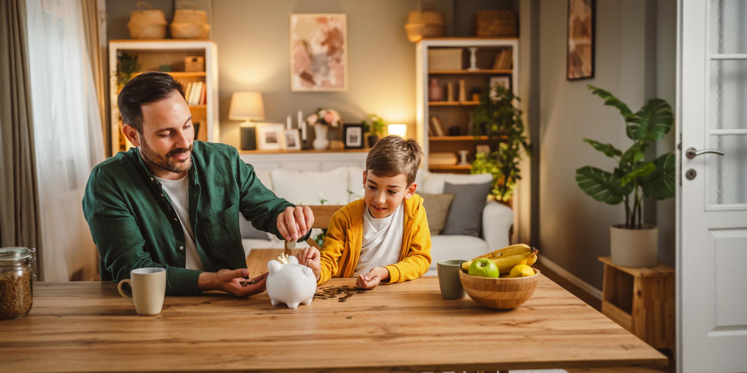 Die Energiepreisbremse hat dich vor zu hohen Kosten geschützt Vater und Sohn sitzen am Tisch im Wohnzimmer und füllen Sparschwein auf