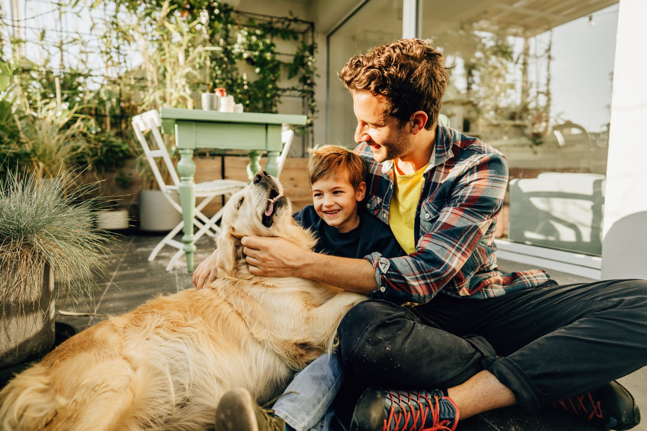 Vater mit Sohn sitzen lachend mit Hund auf der Terasse