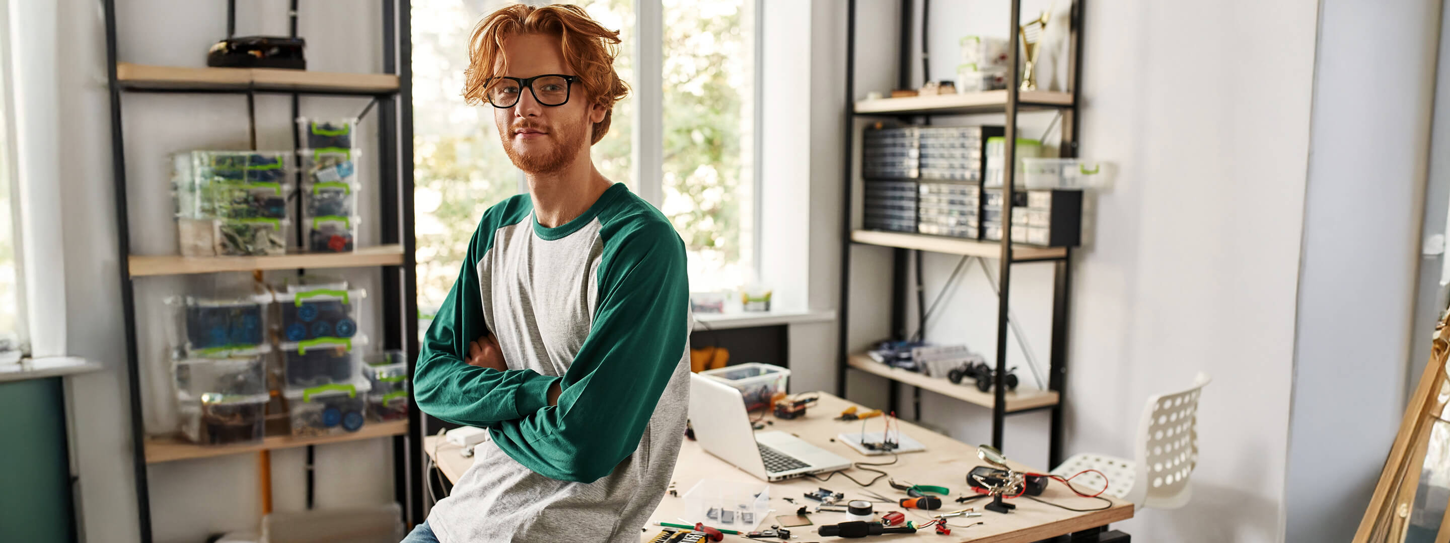 Mann sitzt auf dem Tisch im Home-Office - im Hintergrund sind elektrische Bauteile zu sehen