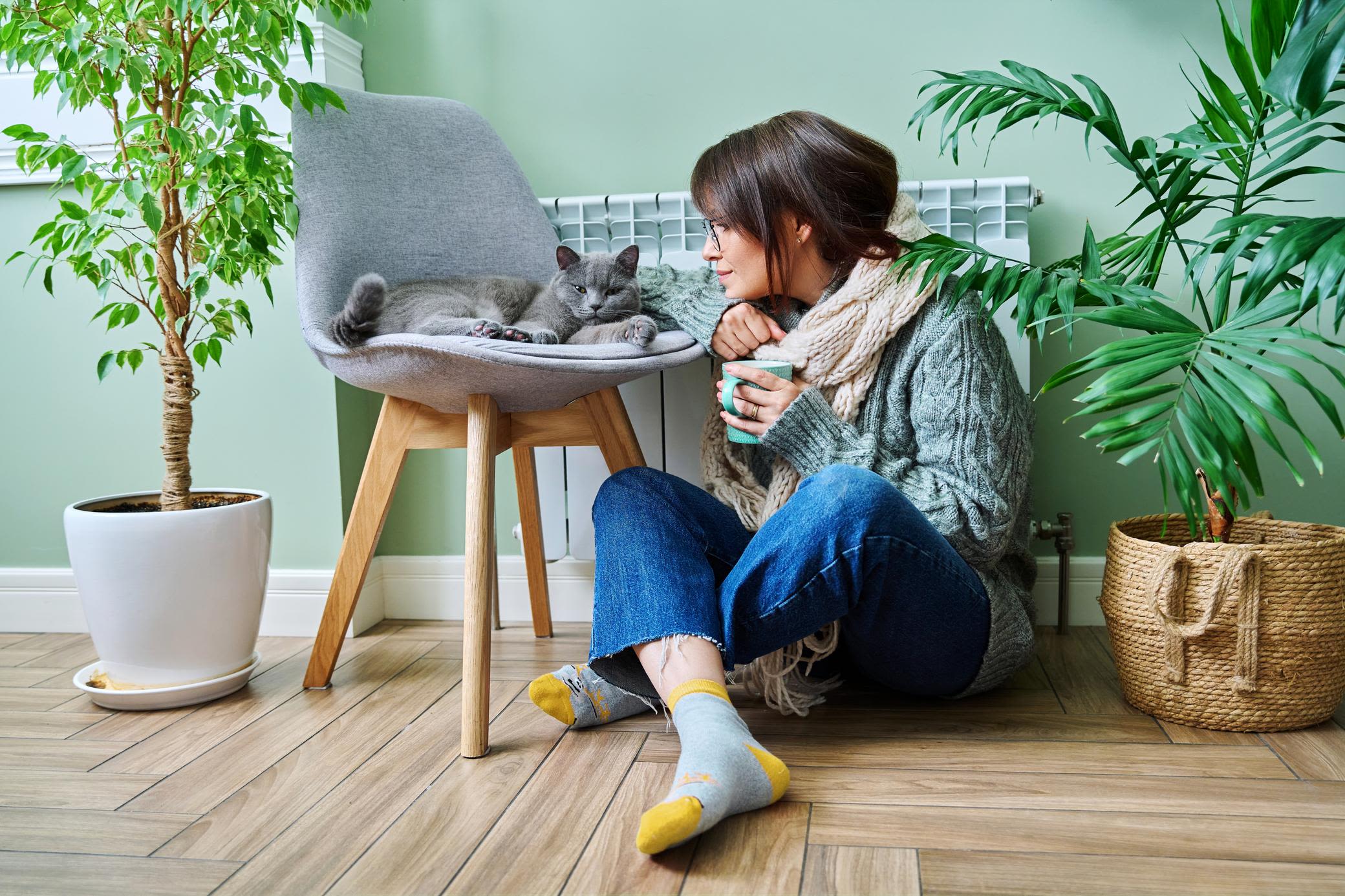 Achte auch in deiner Mietwohnung auf die Heizkosten Frau sitzt in warmer Kleidung mit Katze vor der Heizung