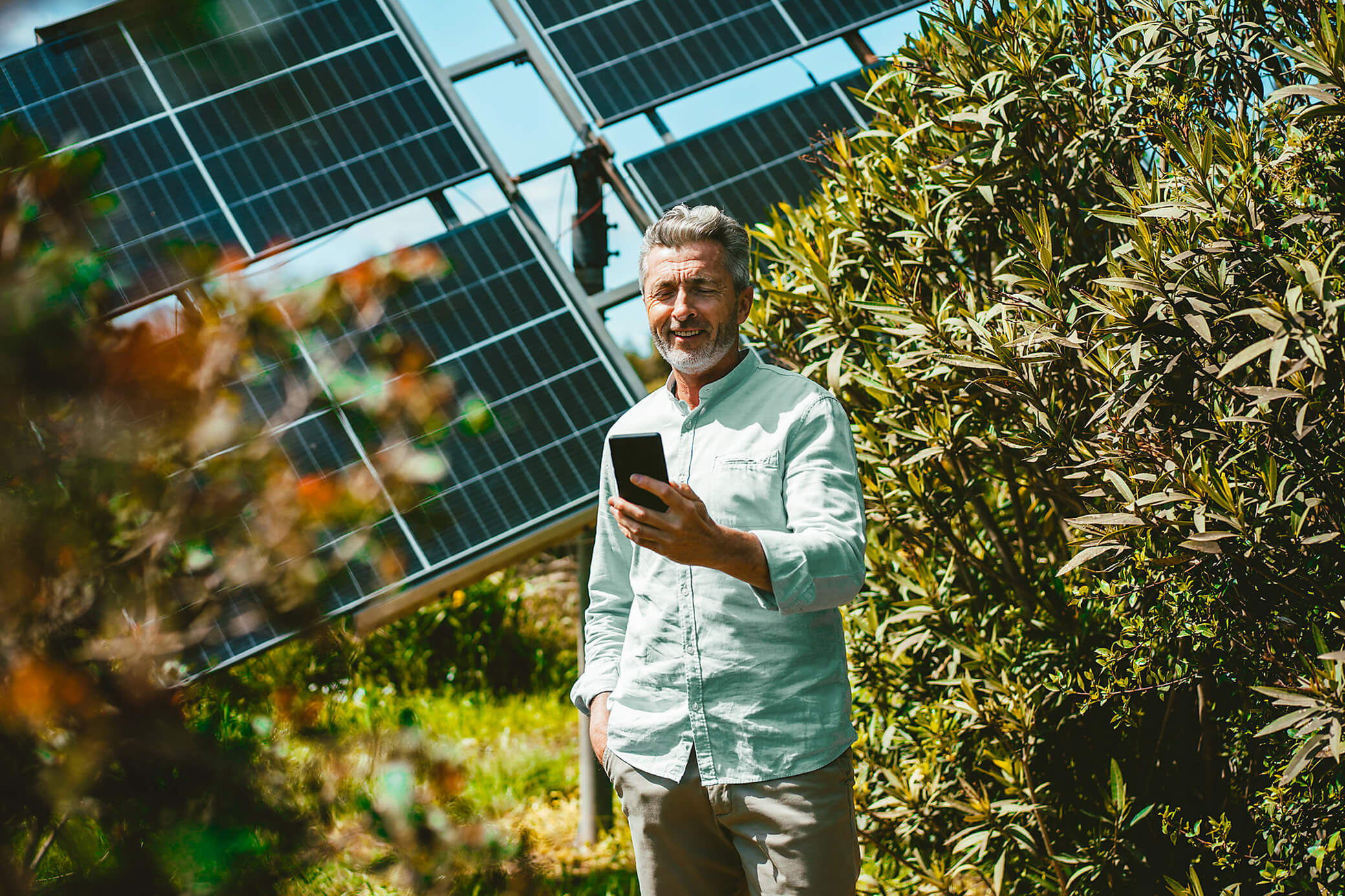 Mann steht mit dem Handy vor einer Solaranlage im Grünen