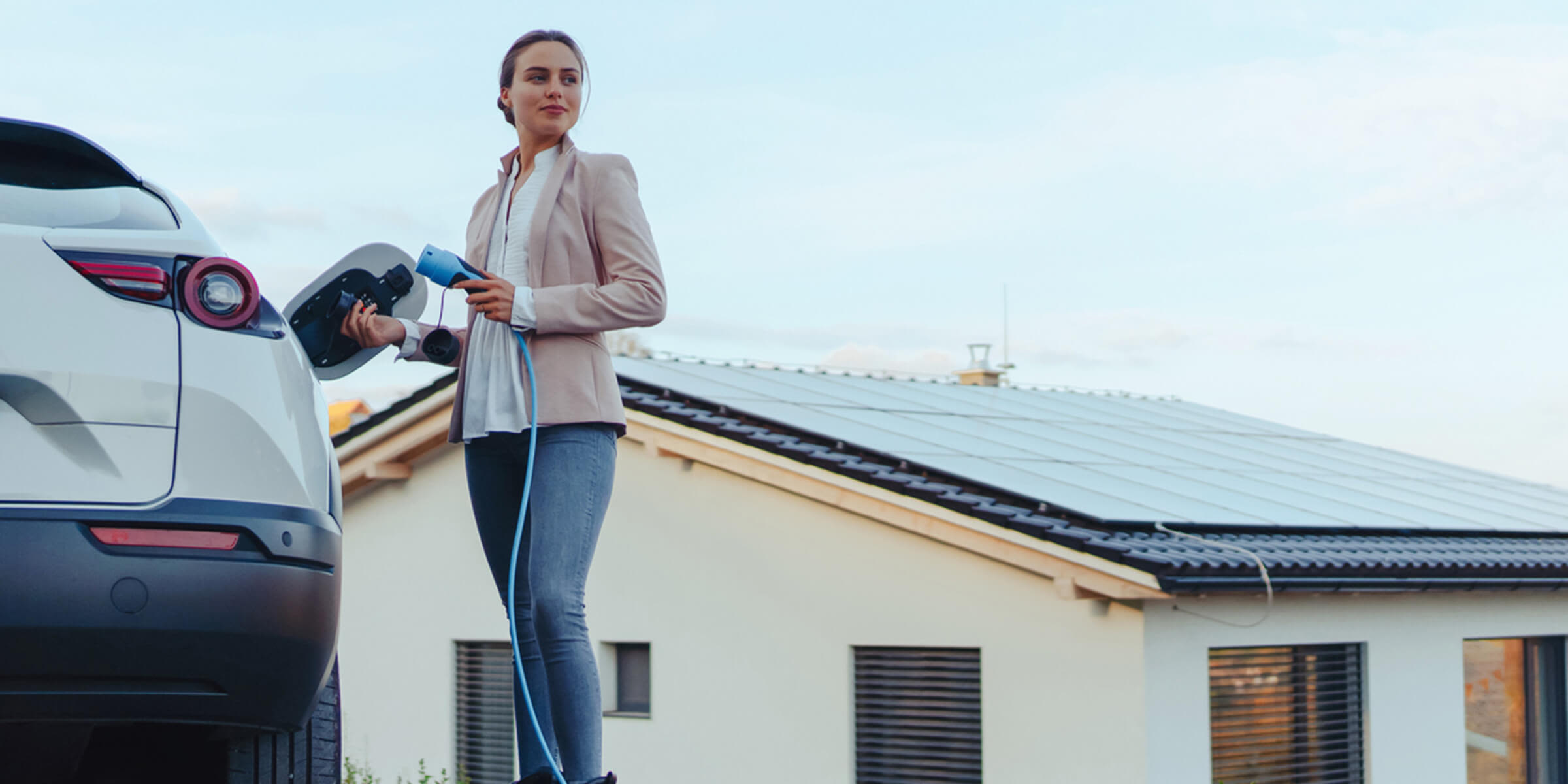 Wallbox, Wärmepumpe, Kühlanlage und Speicher flexibel ins Netz einbinden Frau lädt ihr E-Auto - mit eigener Solaranlage auf dem Dach.