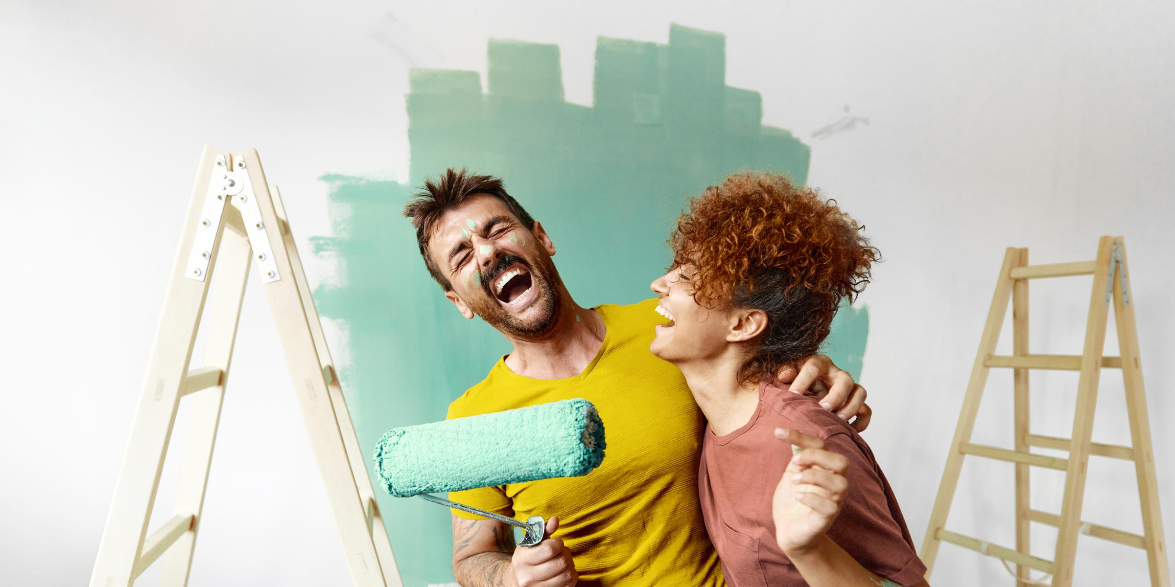 Junges, lachendes Paar streicht die Wohnung grün